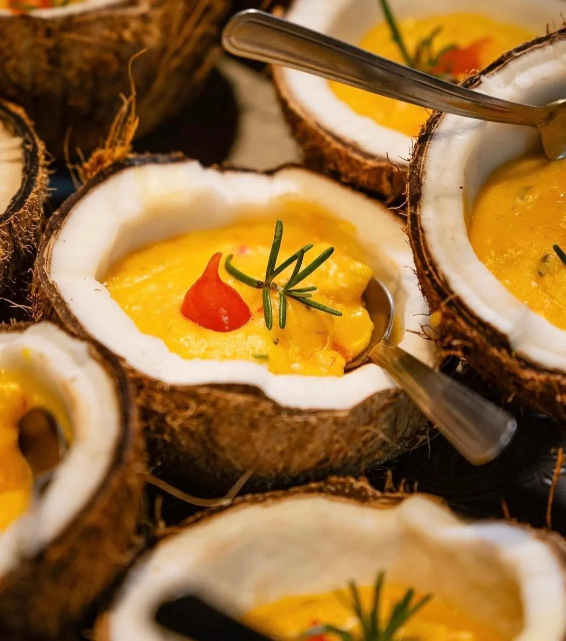 Ovos cozidos servidos dentro de cocos cortados ao meio, decorados com um raminho de alecrim e uma cereja de pimentão.