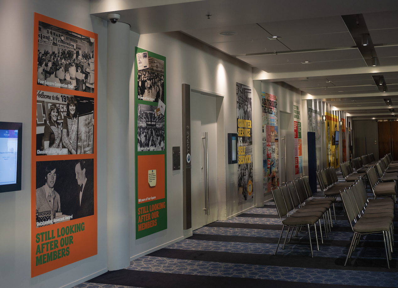 Conference waiting area with chairs and colorful posters on the wall showcasing past events.