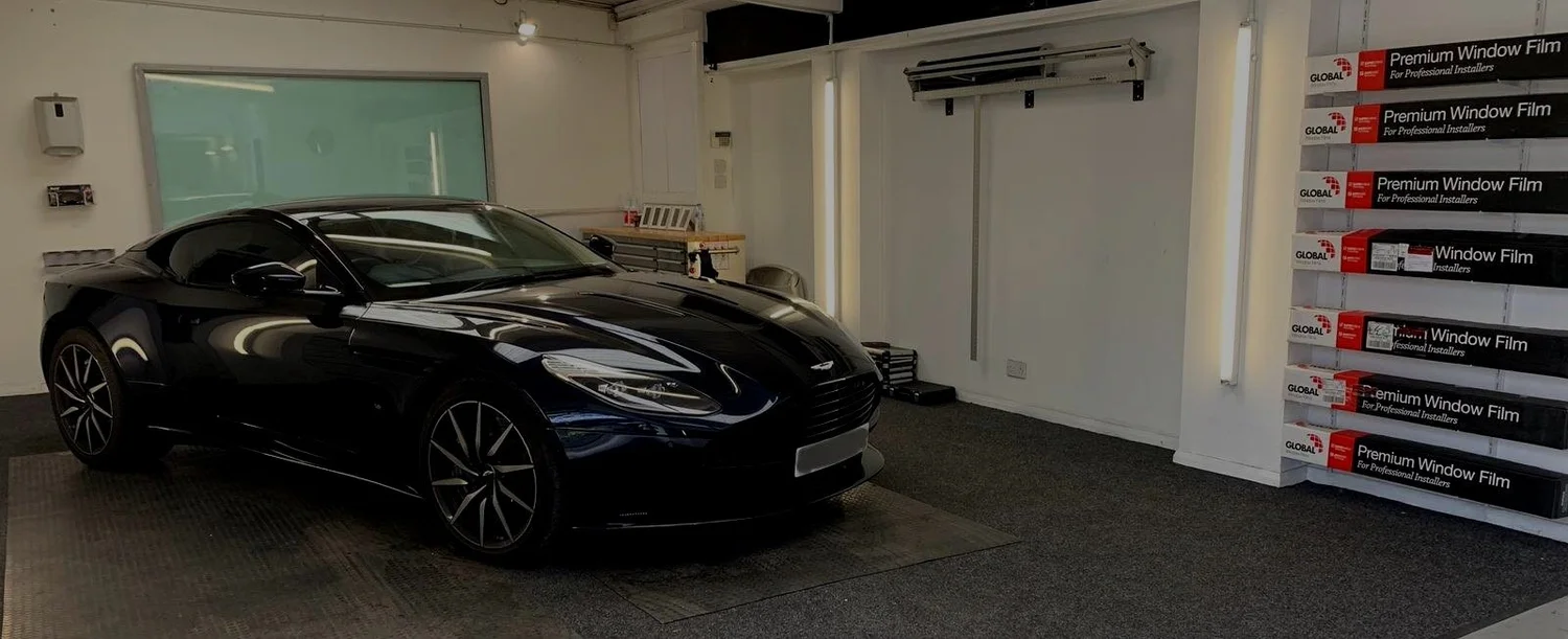 Black Aston Martin in the TintTech Nottingham studio, beside a rack of premium window film