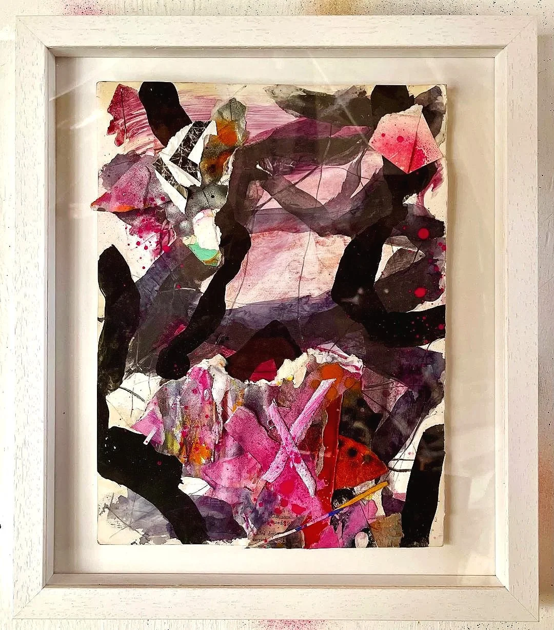 Abstract mixed media artwork with bold black shapes, pink, red, orange, and green splashes, framed in white