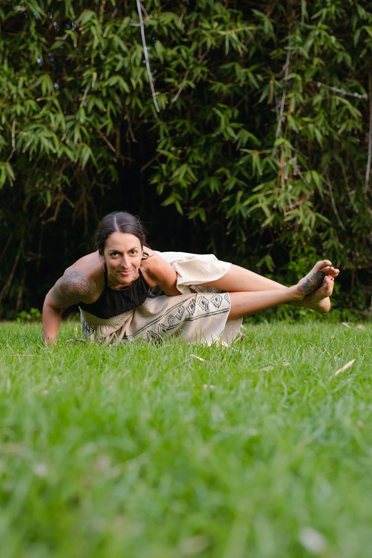 Woman practicing yoga outdoors on green grass with tall bushes in the background.