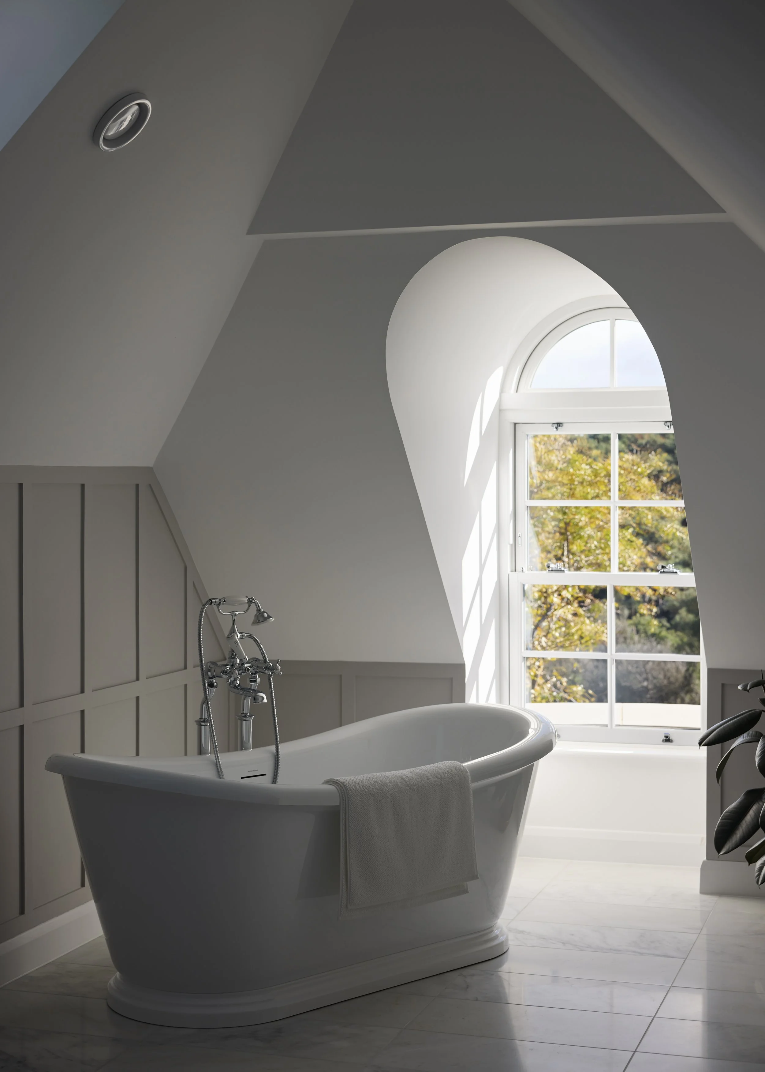 Bathroom at Over Links with a freestanding bath beneath an arched window and pitched ceiling