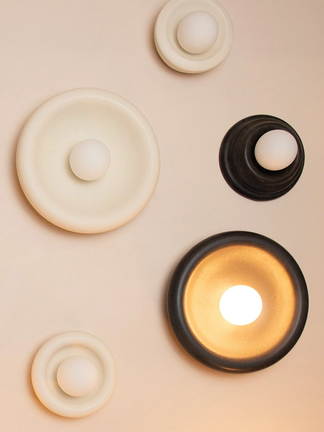Decorative wall lights in black and white, with round shapes and warm and white lighting on a beige wall.