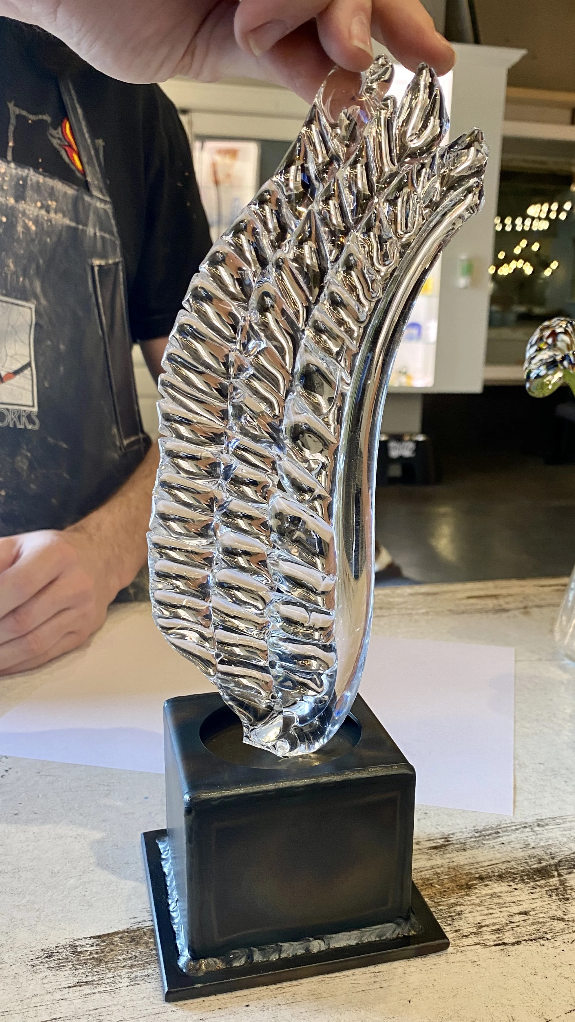 A person holding a glass sculpture resembling a wing on a black base.