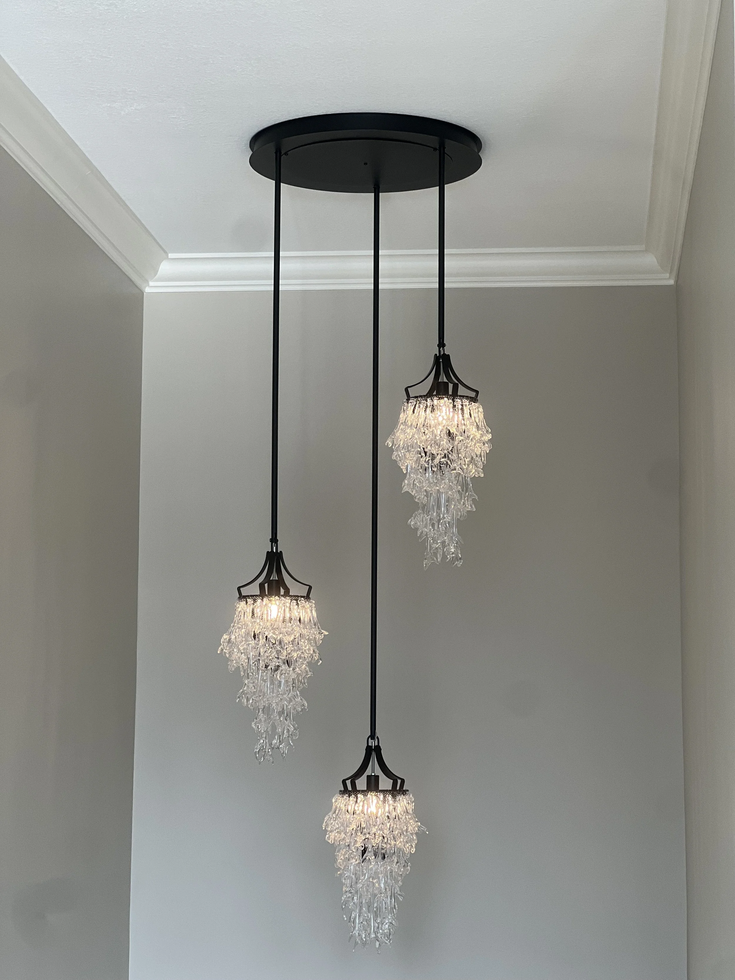 Modern chandelier with three glass pendant lights hanging from a black ceiling mount in a room with white walls and crown molding.