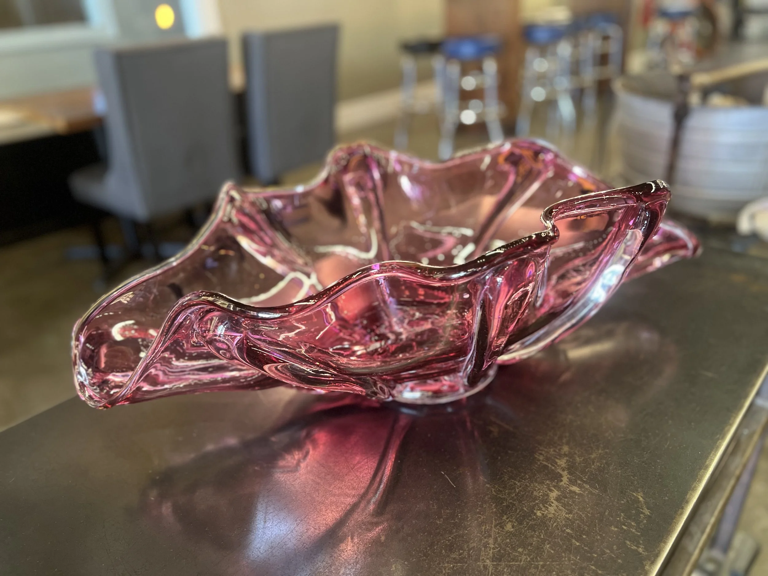 A pink glass decorative bowl with a wavy, ruffled scalloped edge on a dark surface.
