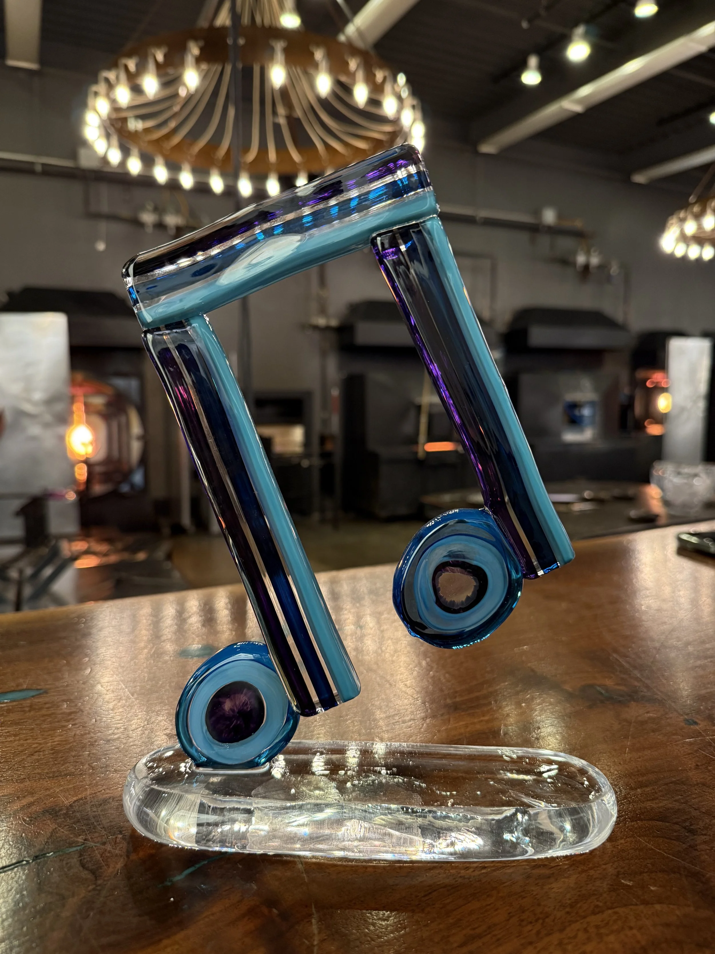 Colorful glass sculpture resembling a musical note on a wooden table in a modern interior with decorative lighting.