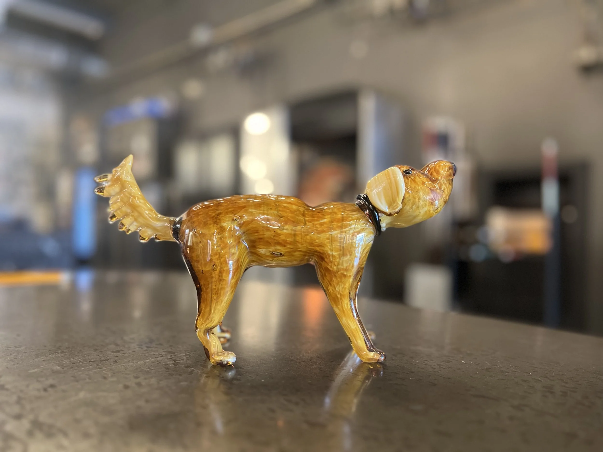 Glass figurine of a dog with a collar, placed on a dark countertop with a blurred studio background.