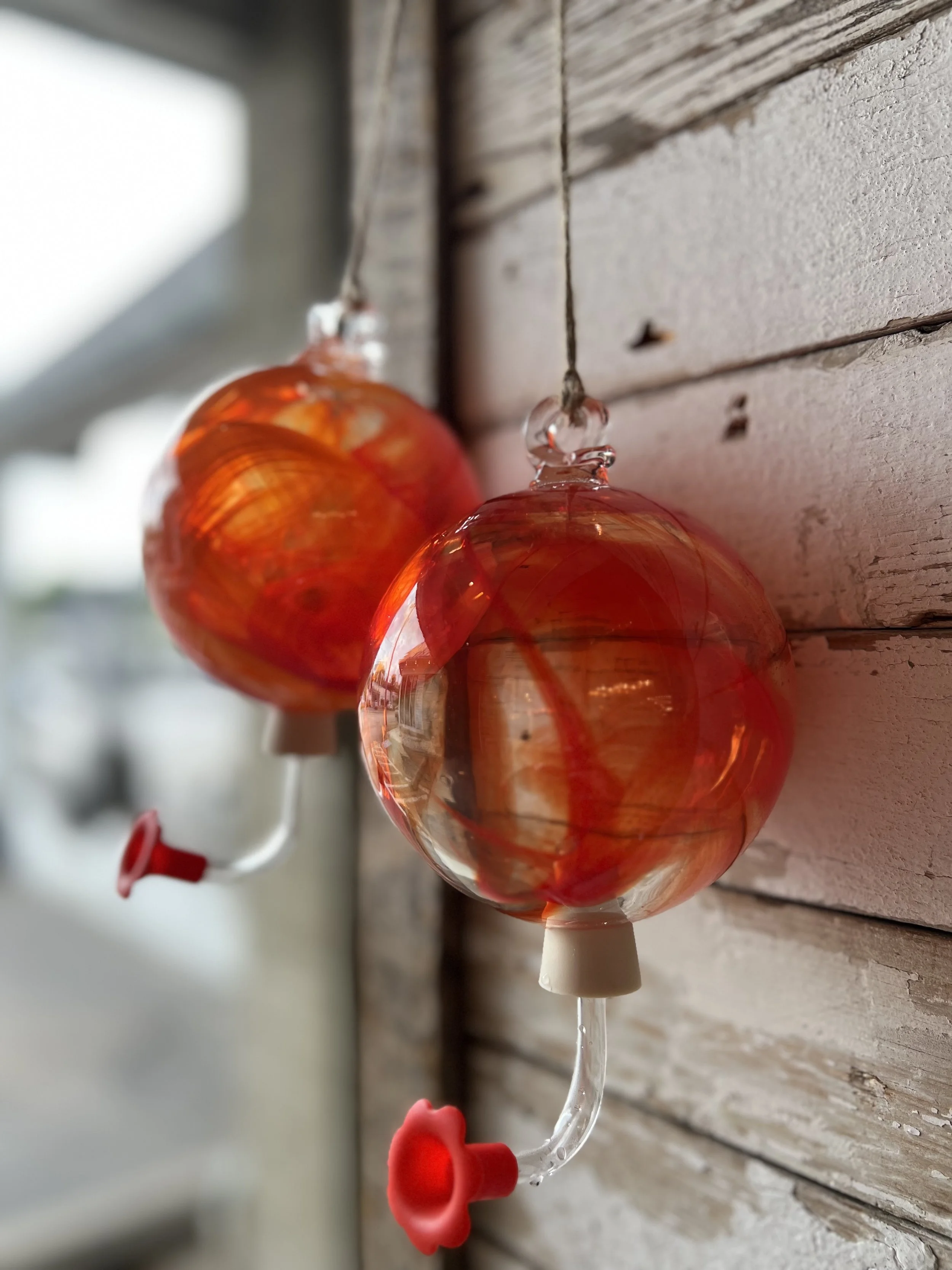 Two red glass hummingbird feeders hanging on a wooden wall.