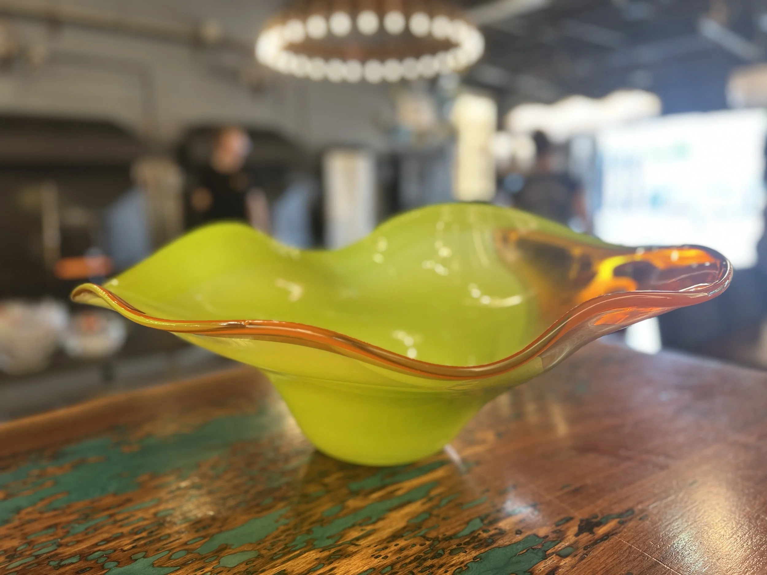 A green glass sculpture with an orange and red rim, placed on a wooden surface in an industrial setting.
