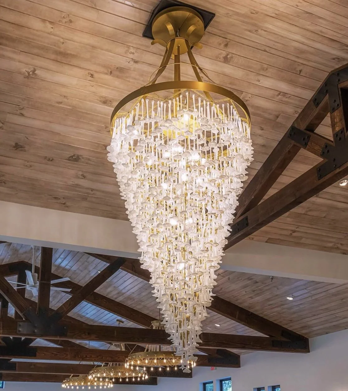 Elegant chandelier with white flower-like decorations hanging from a gold ring in a wooden ceiling room.
