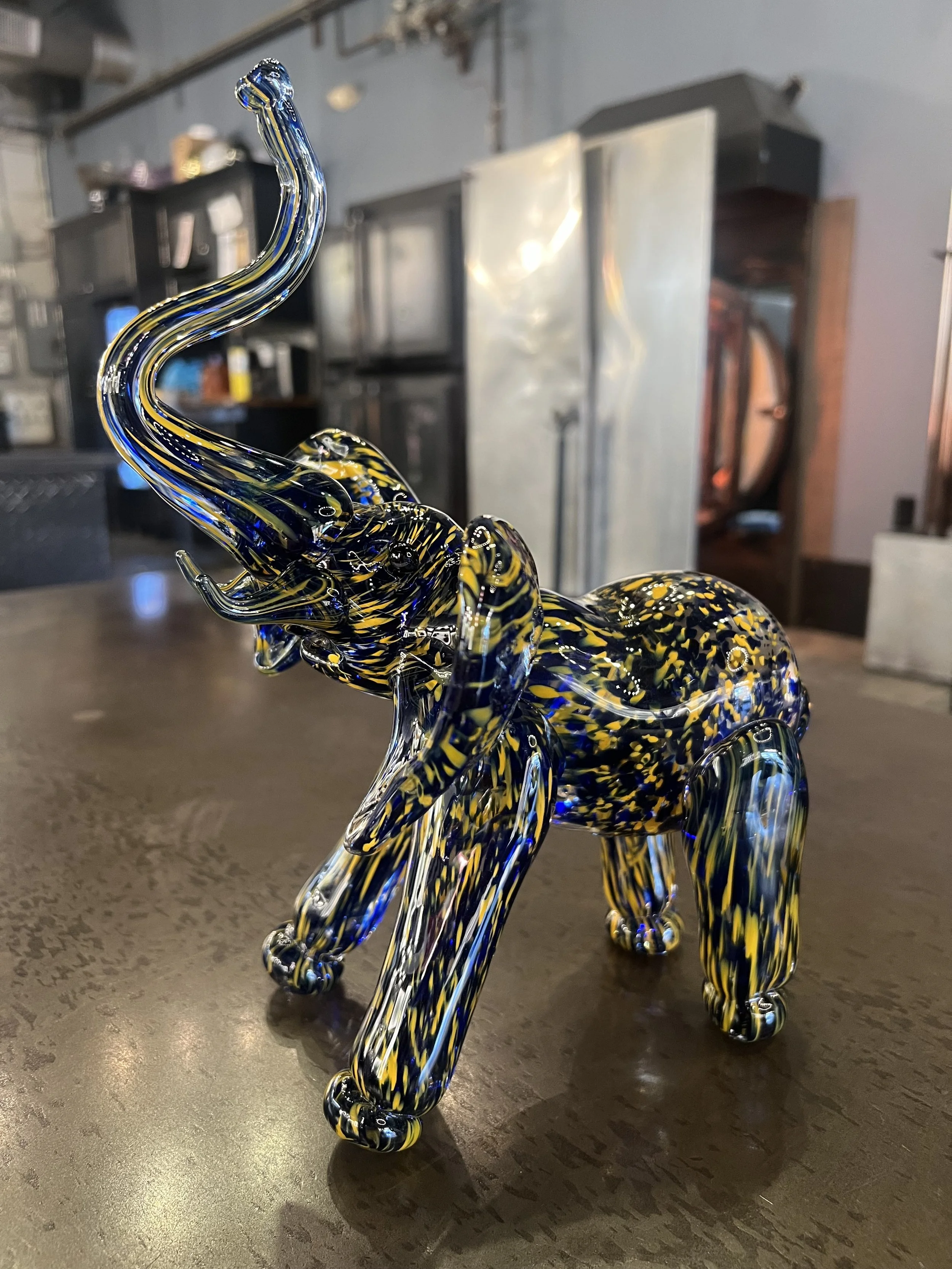 Colorful glass elephant sculpture with swirls of blue, yellow, and black on a dark wooden surface.