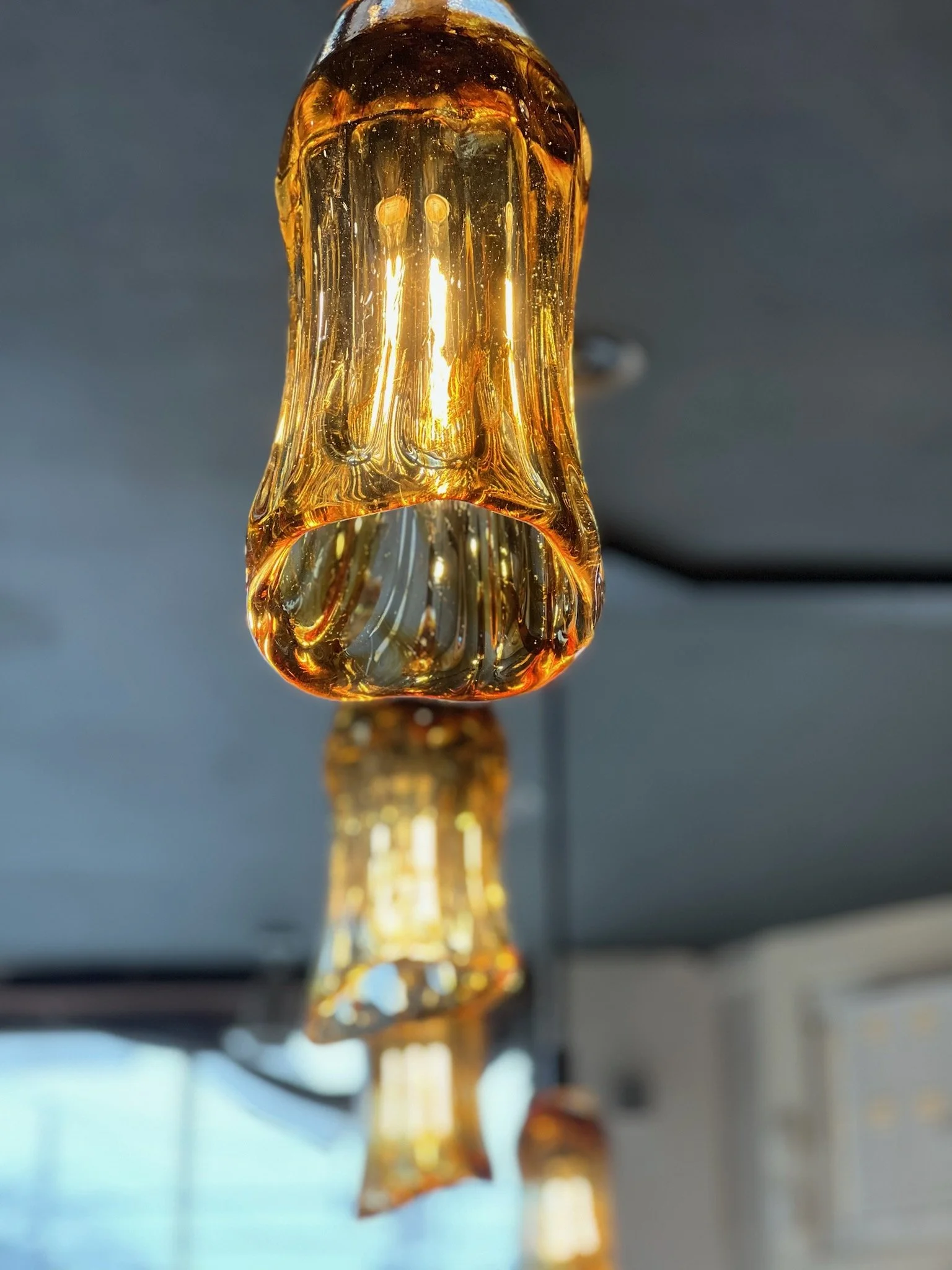 Close-up of a glass light fixture with warm amber tones hanging from the ceiling, with a blurred background.