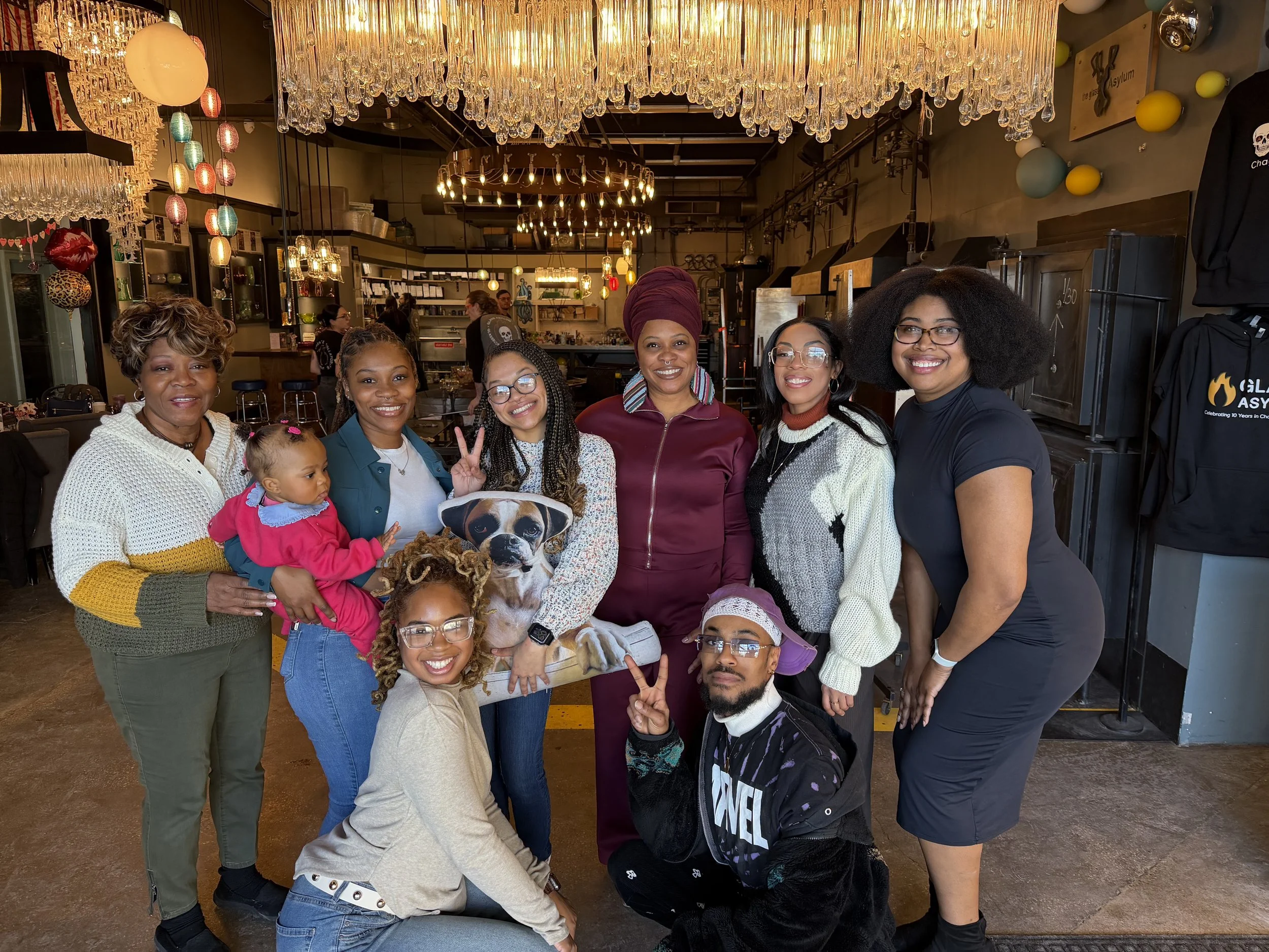 Group enjoying themselves during a glassblowing workshop taking a family photo under chandelier