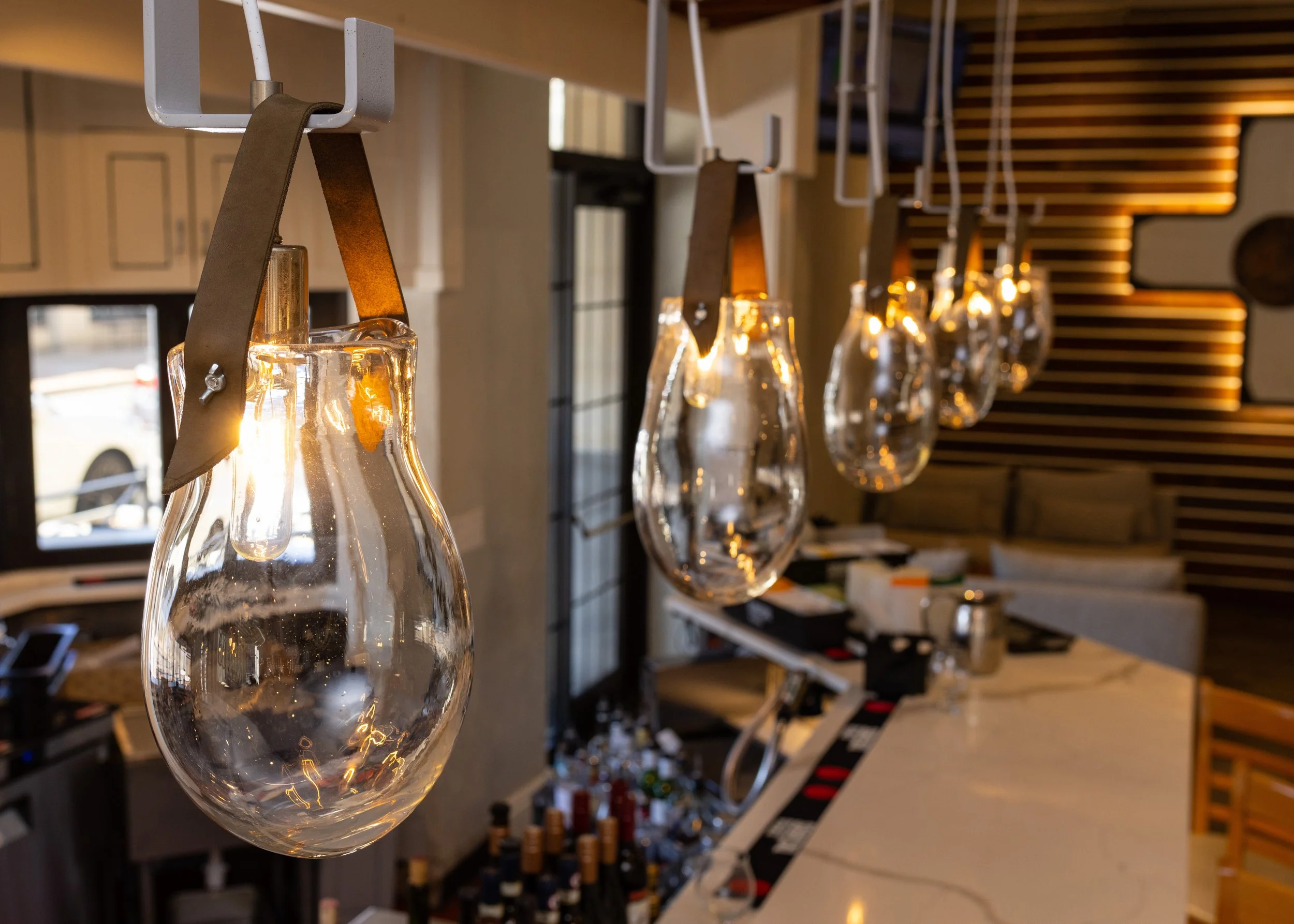 Decorative containers made of glass hanging from leather straps over a bar or counter in a modern restaurant or bar interior.