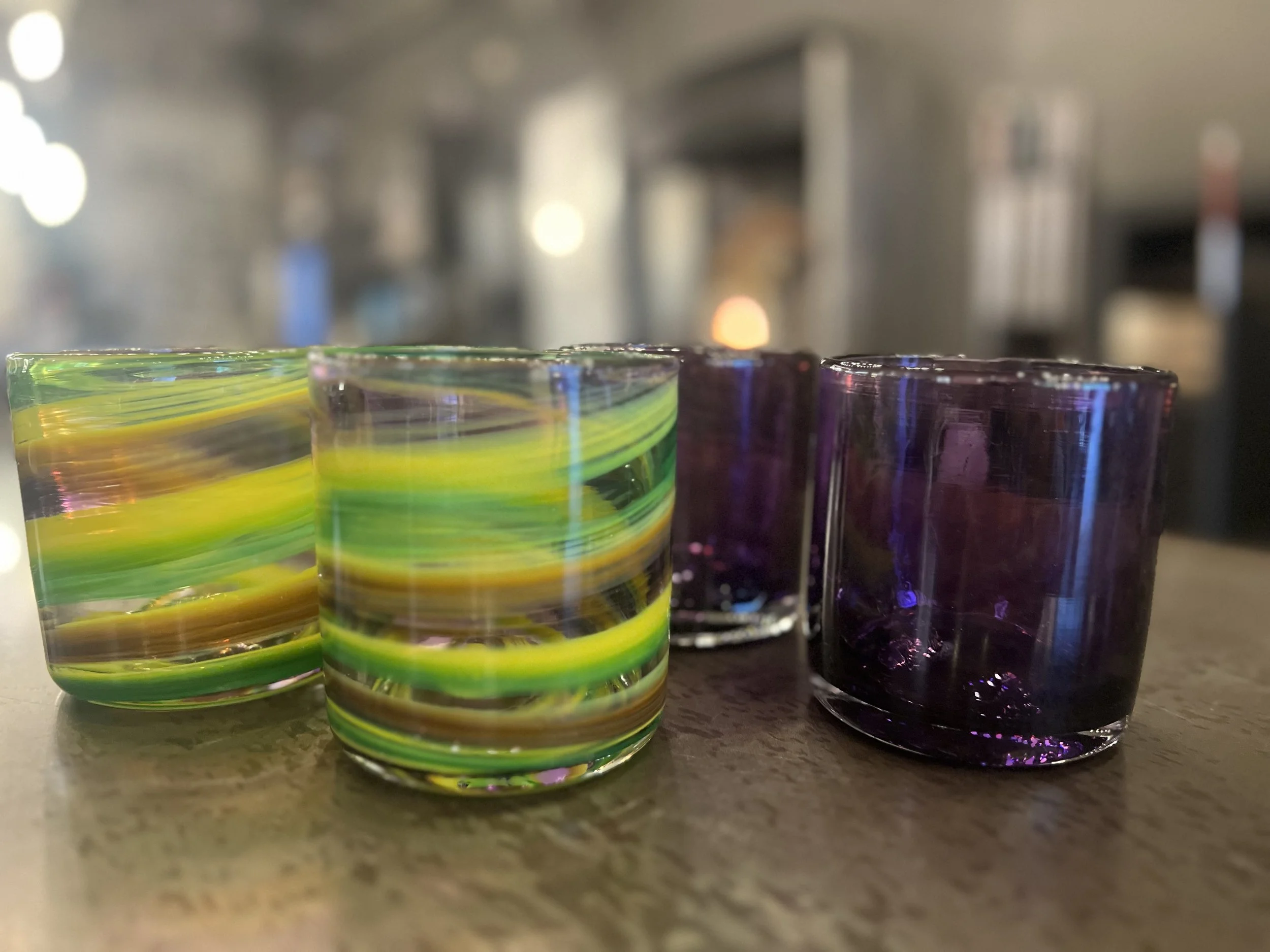 Four colorful glass cups with swirling yellow, green, and purple patterns on a wooden surface.