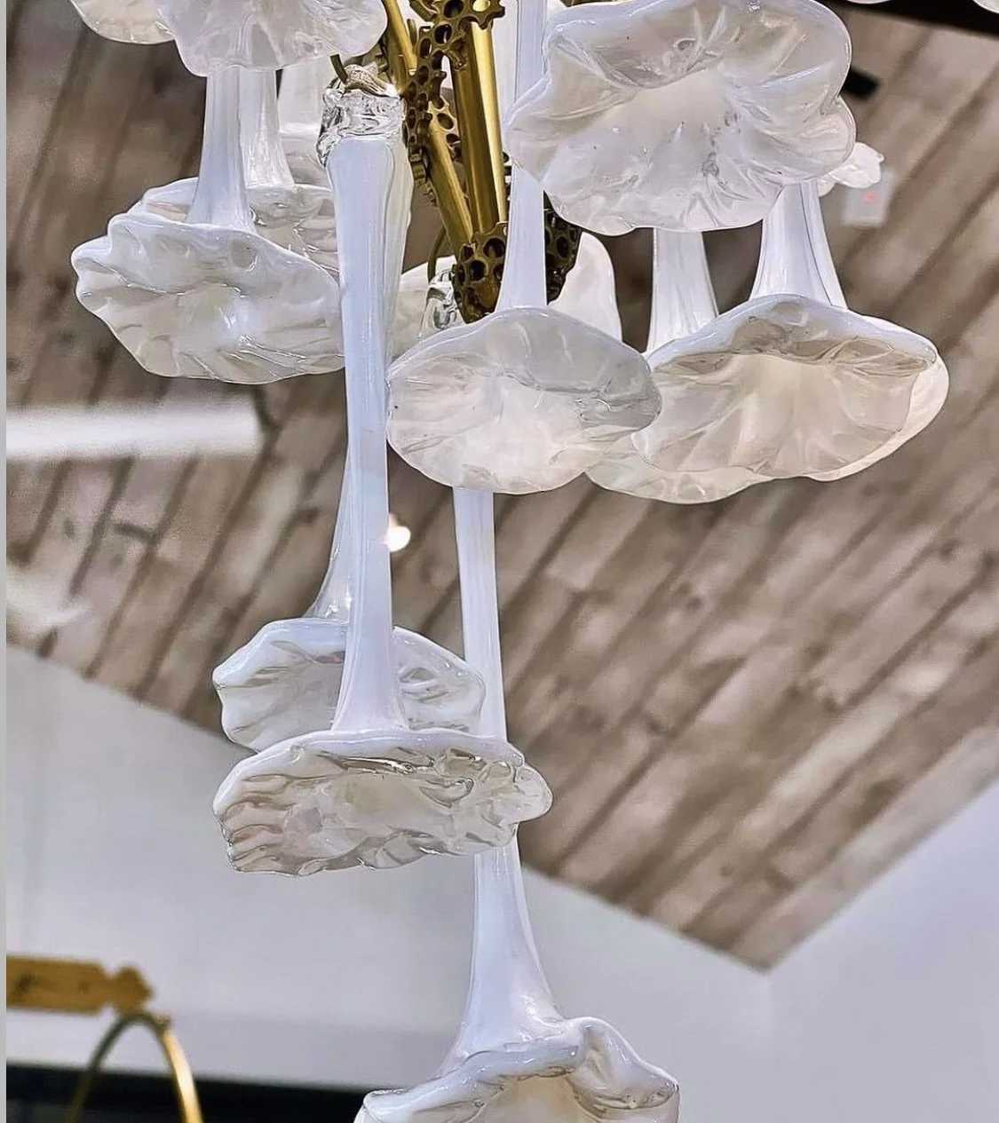 Close-up of a decorative chandelier with carved glass or resin flower-like elements hanging from gold-colored rods, against a wooden ceiling background.