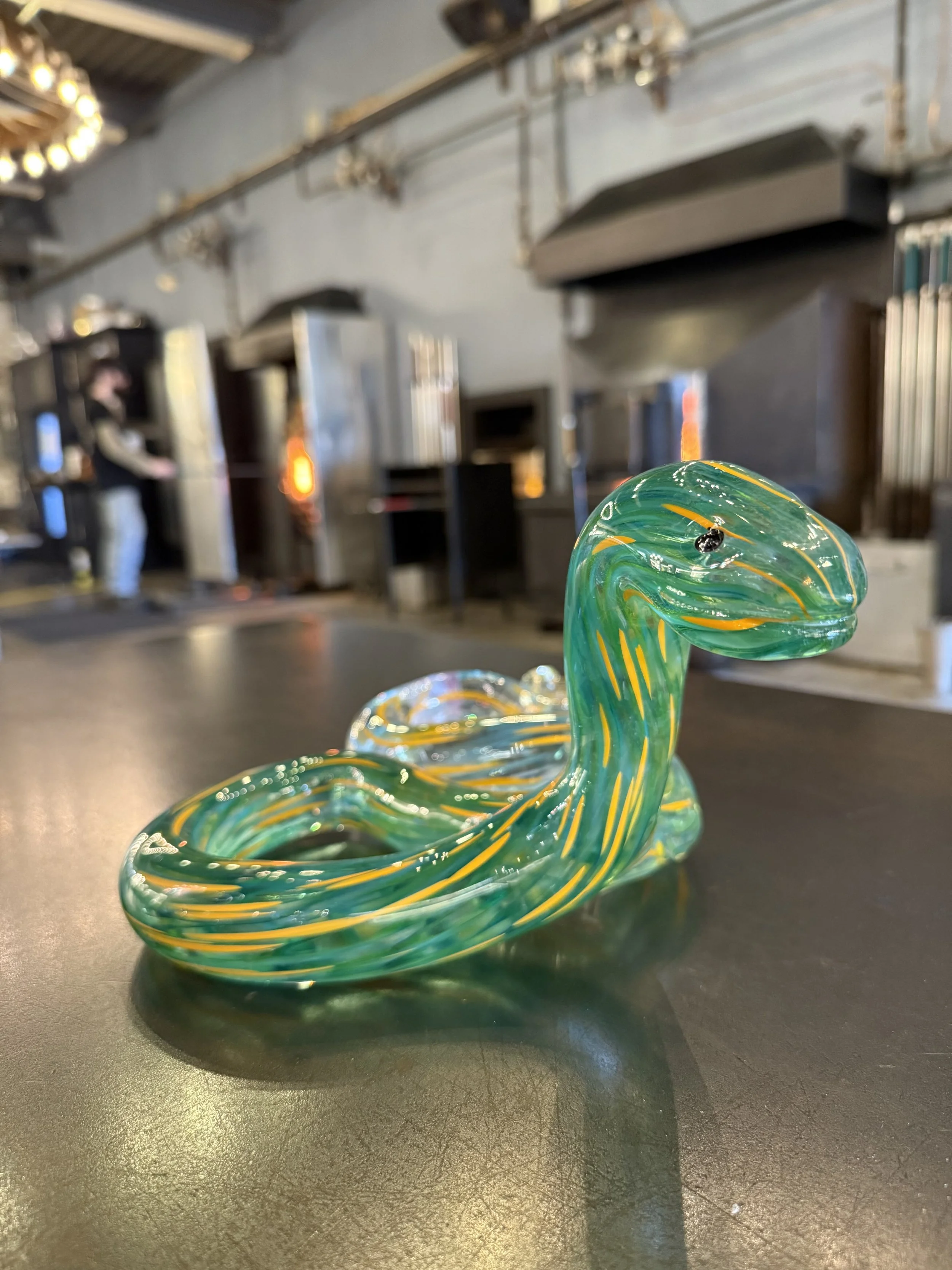 A glass swirl decoration resembling a snake, predominantly green with yellow accents, placed on a black surface in a modern industrial interior.