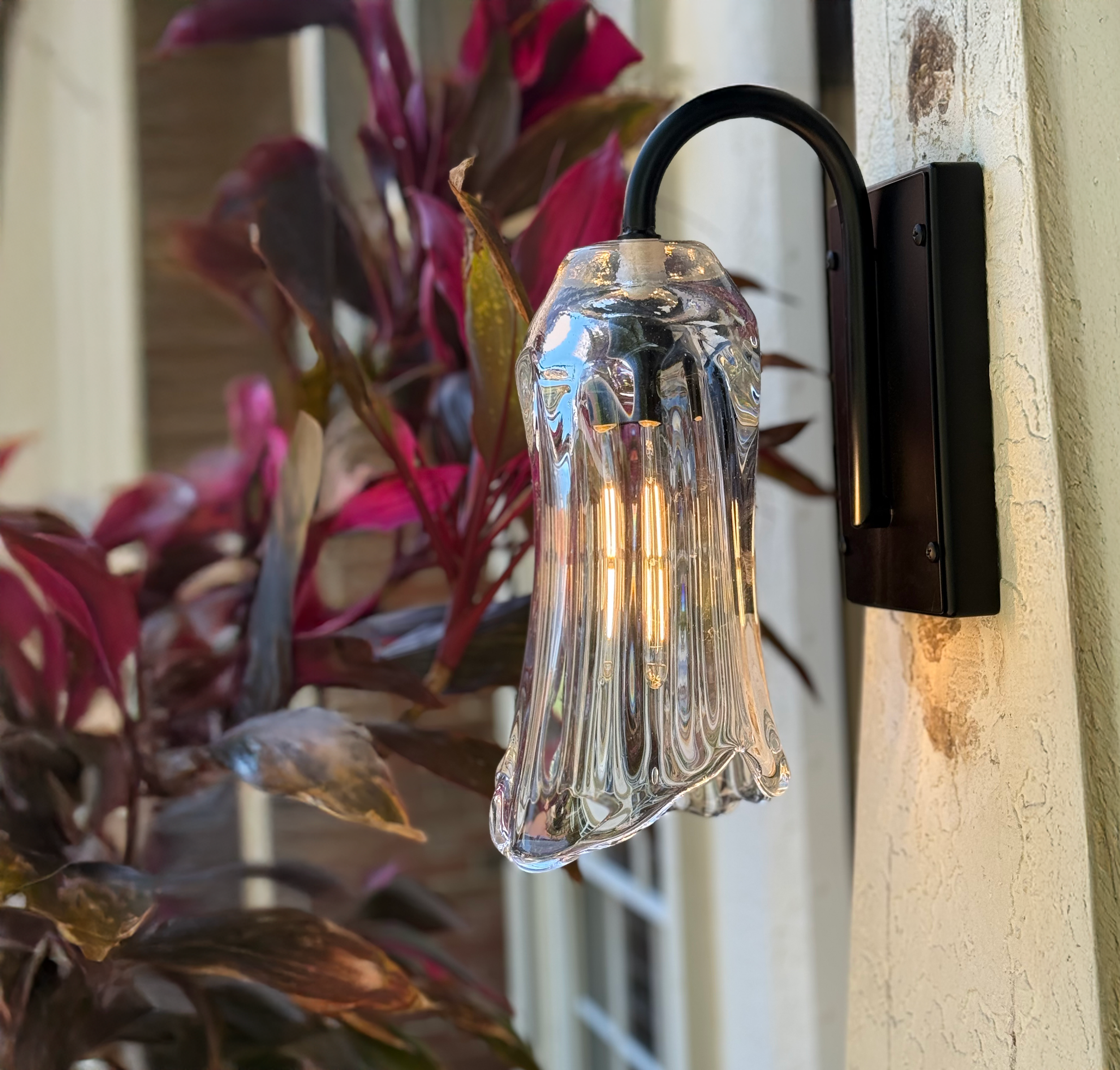 Glass wall sconce with a flared, bell-shaped shade mounted on a black metal arm.