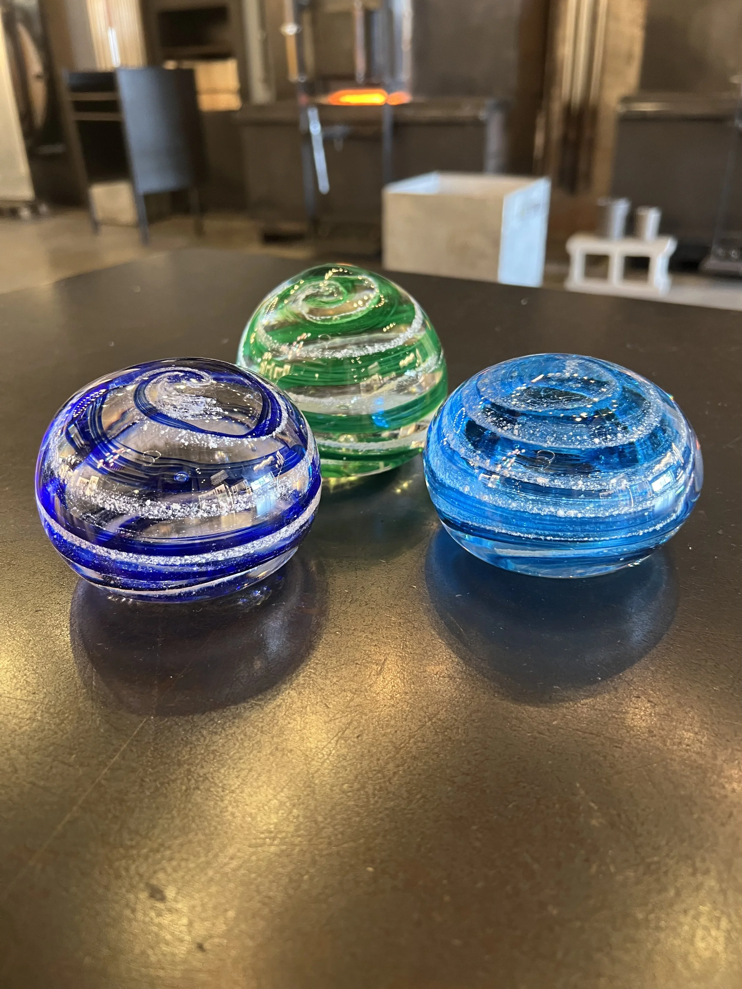 Three glass marbles in blue, green, and clear colors with swirl patterns, placed on a black surface.