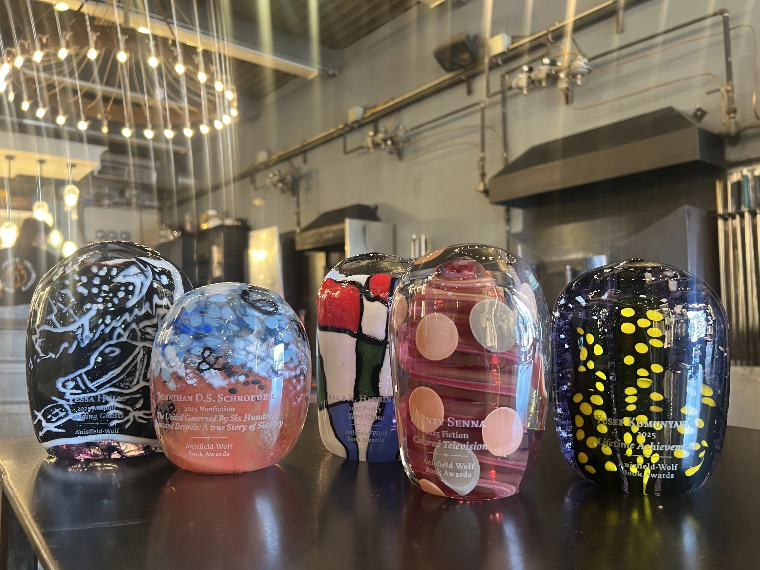 Five decorated glass paperweights with various designs and colors on a black surface in a dimly lit industrial-style room.