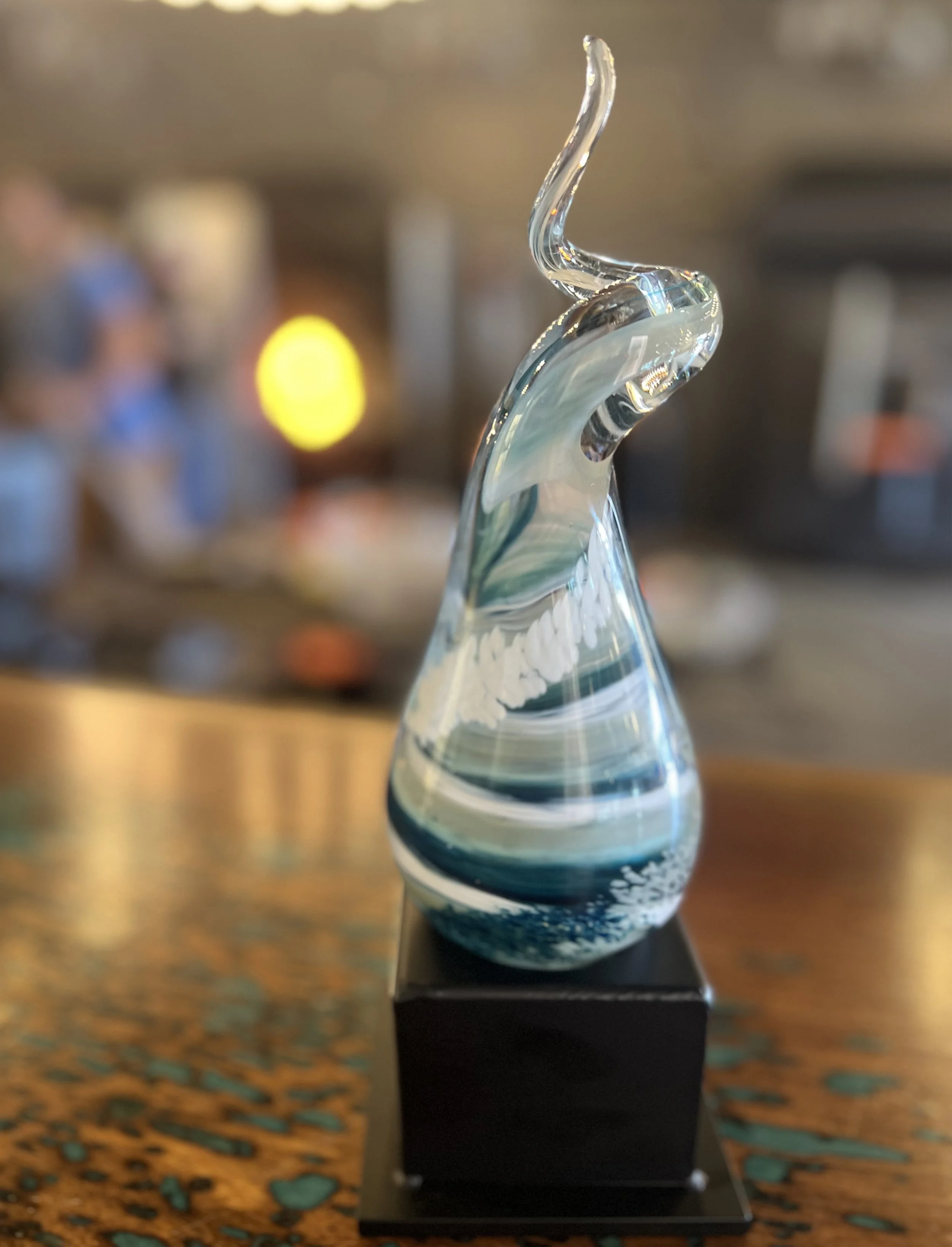 Glass sculpture with a twisted, abstract design on a black base, placed on a wooden surface.