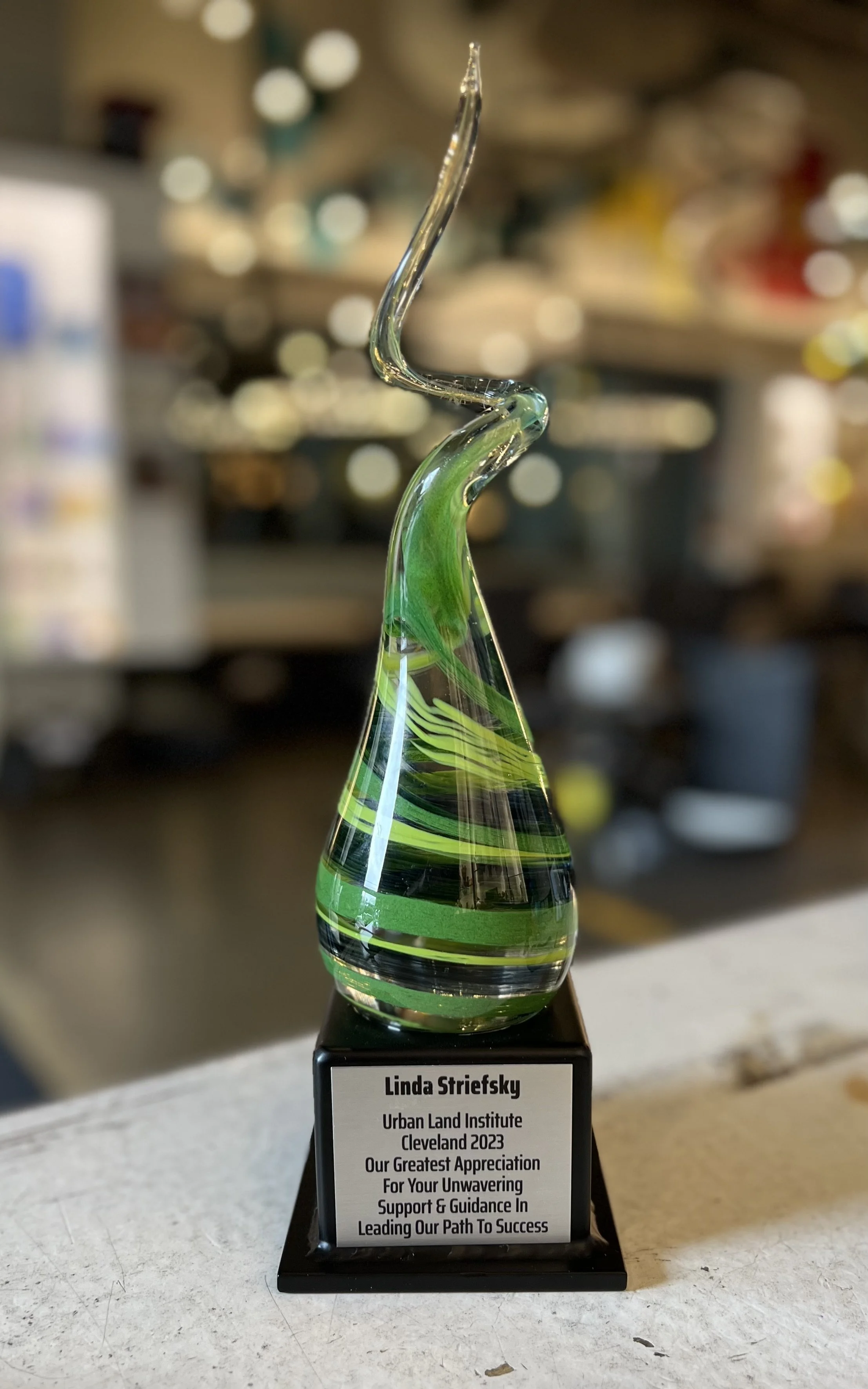 Glass award with a green swirl design on a black base, with a white plaque expressing appreciation for support and guidance, awarded to Linda Striefsky at the Urban Land Institute Cleveland 2023.