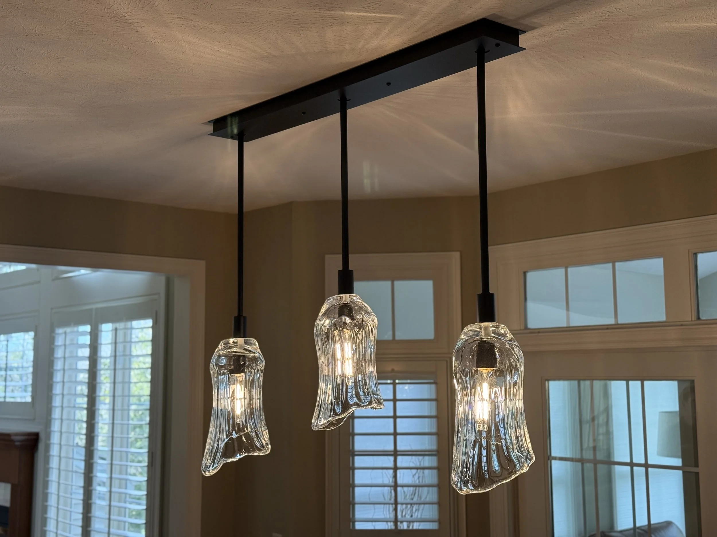 Three pendant lights with glass shades hanging from a ceiling over a room with large windows.