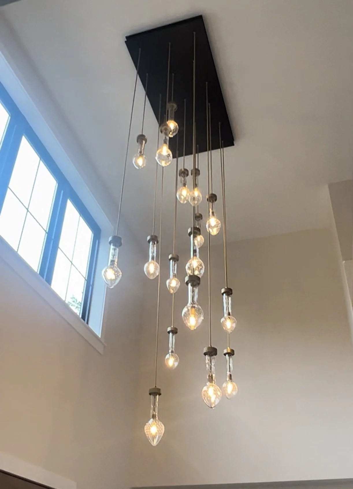 A modern chandelier with multiple hanging bulbs in a home interior near a window.