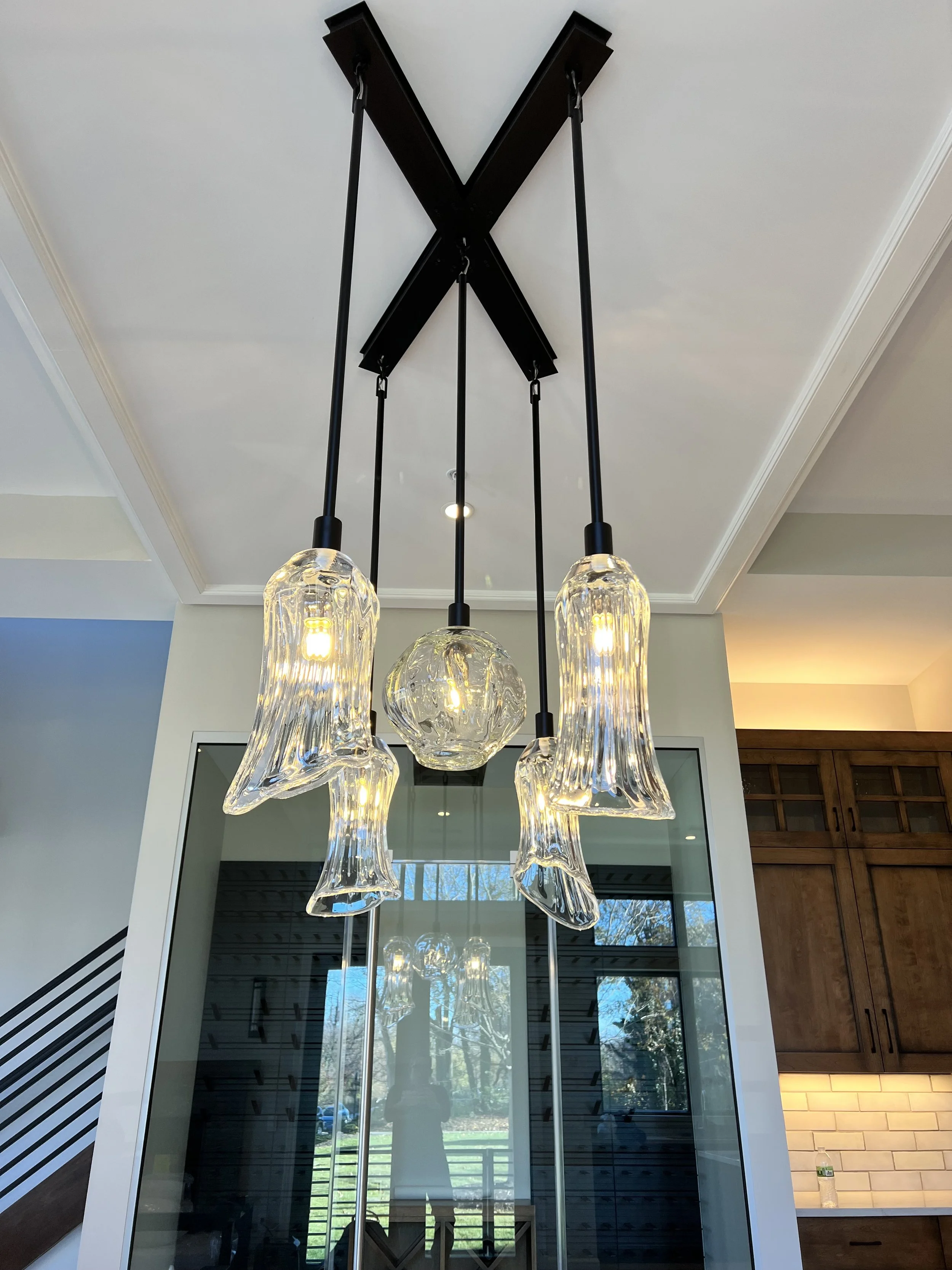 Contemporary hanging light fixture with three glass pendants and a central glass orb, suspended from a black ceiling mount, in a modern interior space.