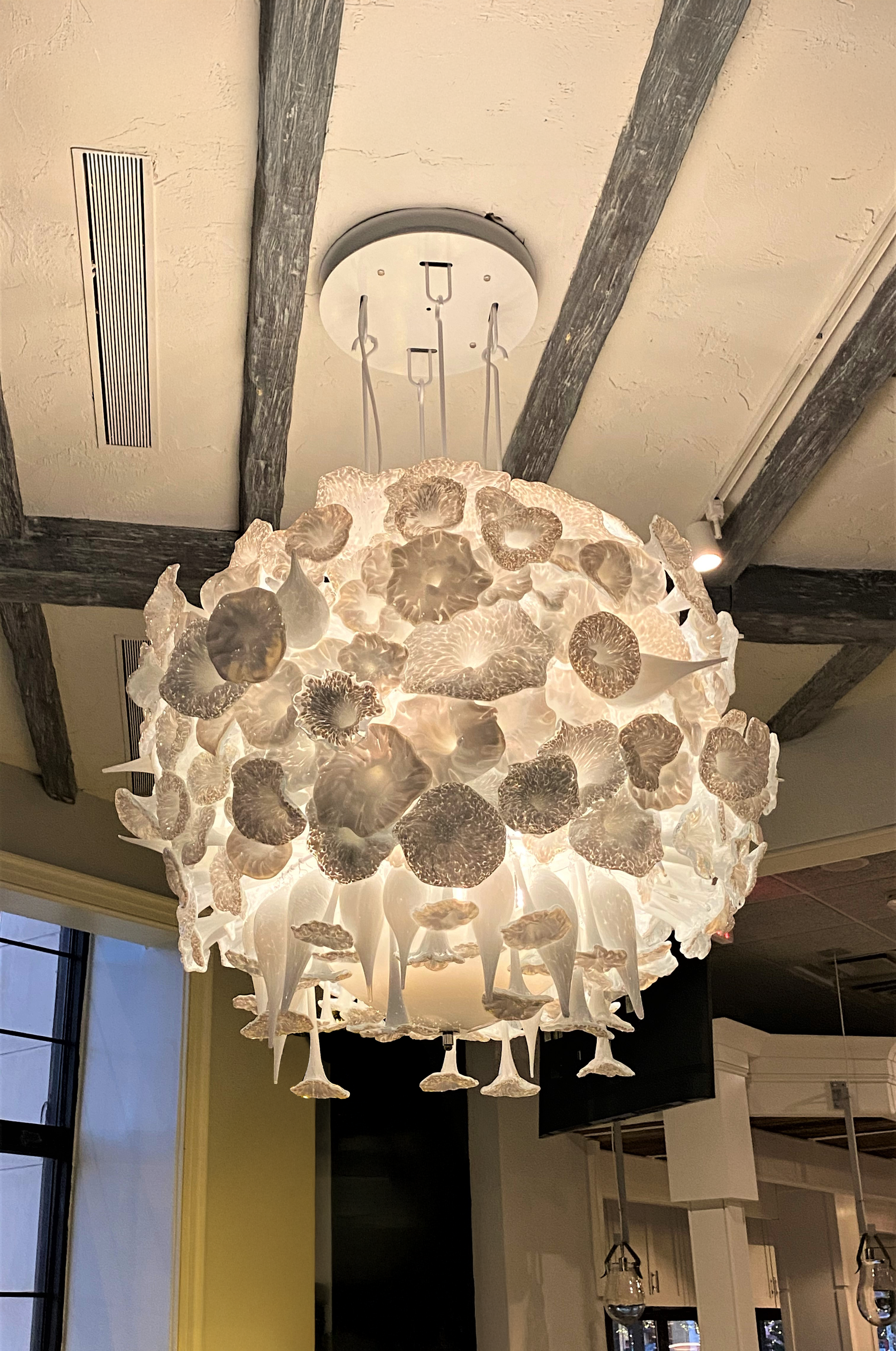 A decorative white chandelier with a floral design, hanging from a ceiling with wooden beams.