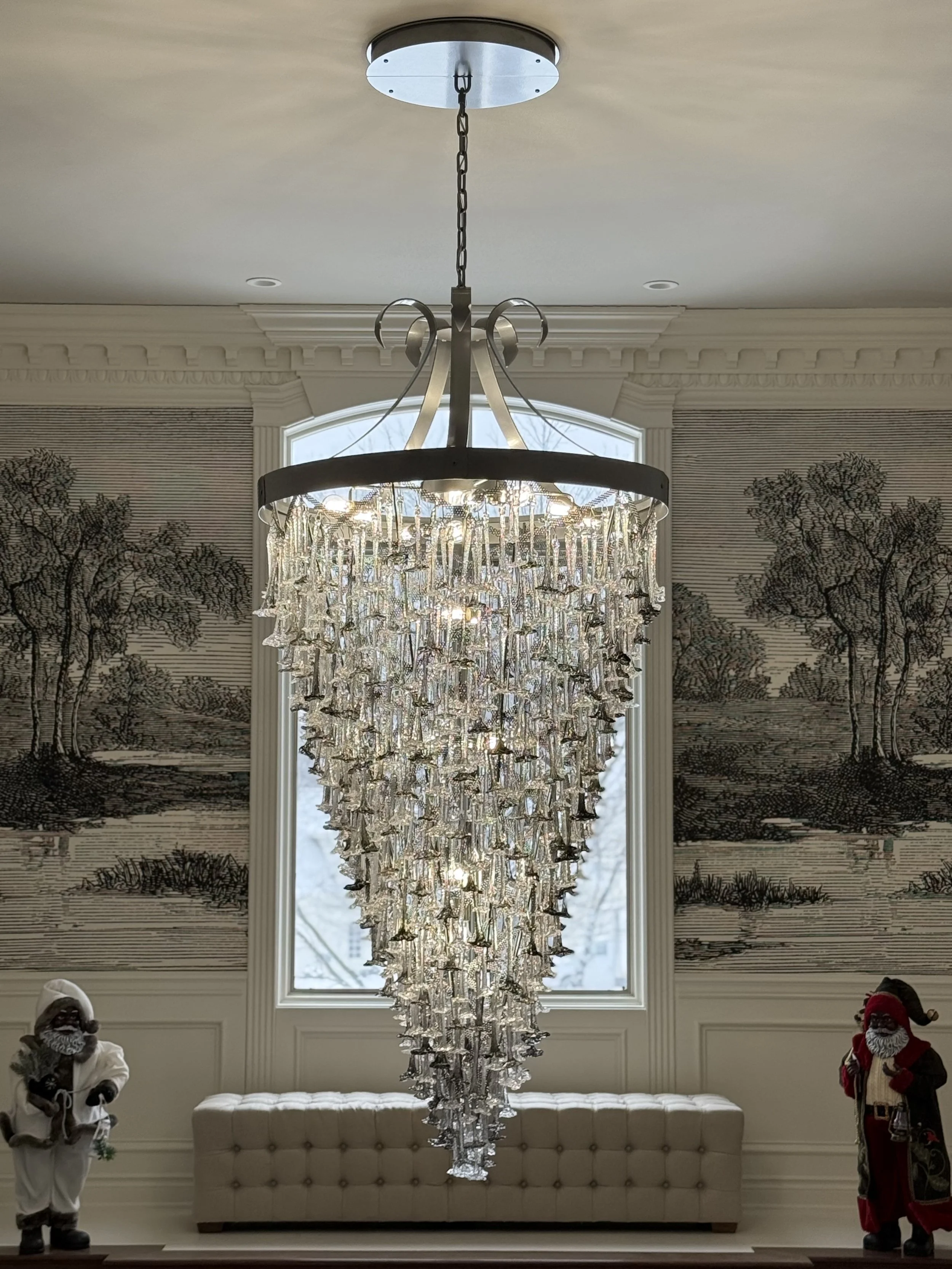 Large chandelier hanging from ceiling in a decorated room with wall murals and holiday figurines.