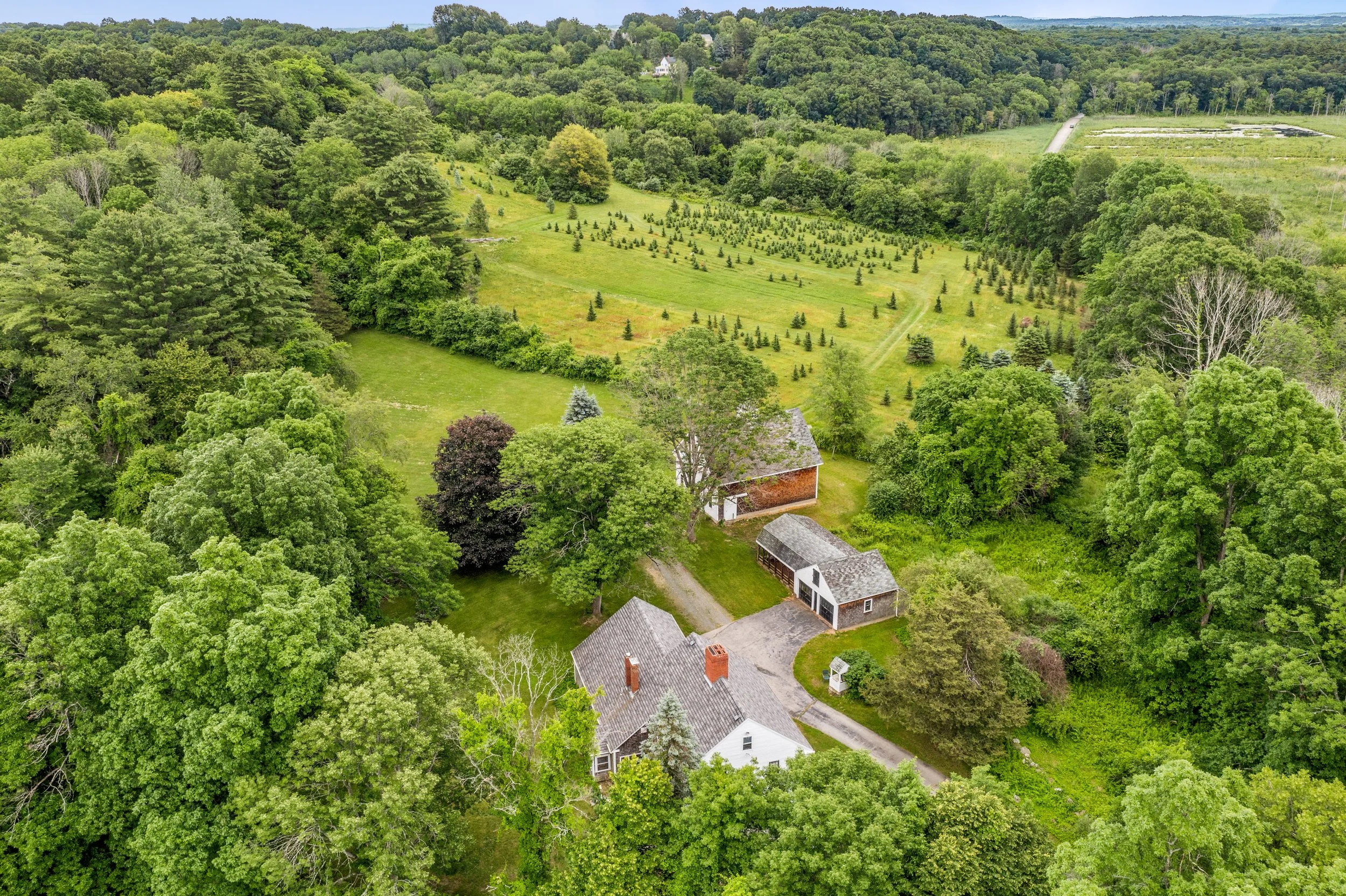 sky view of evergreen farm with farmhouse and trees in the distance