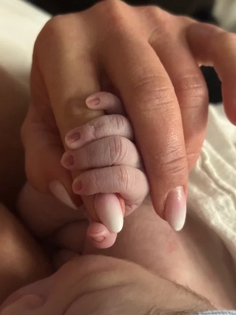 A close-up of a baby’s tiny hand gripping an adult’s finger.