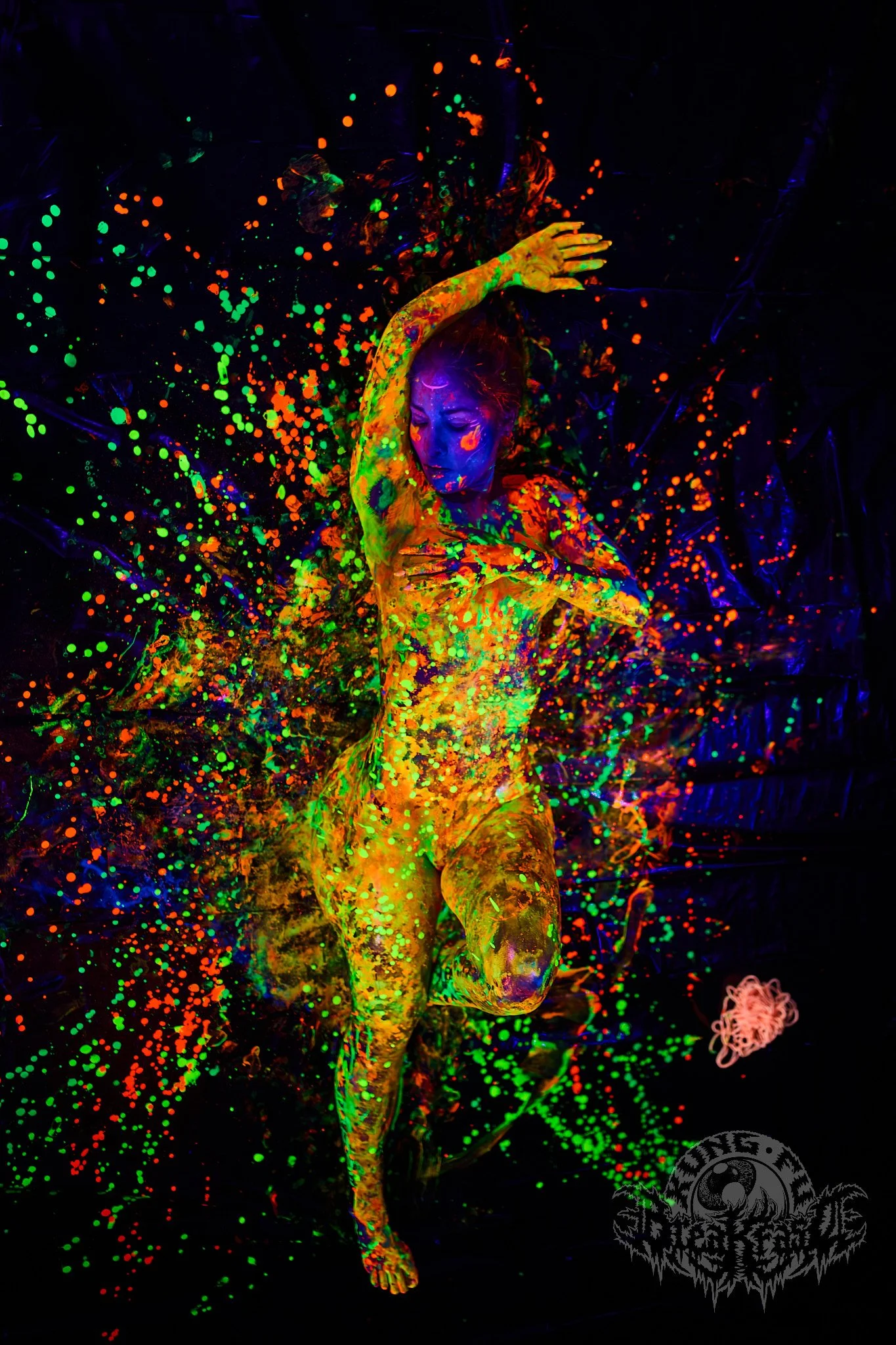 Evy Duarte illuminated by ultraviolet light, surrounded by vibrant fluorescent body paint in a dramatic portrait.