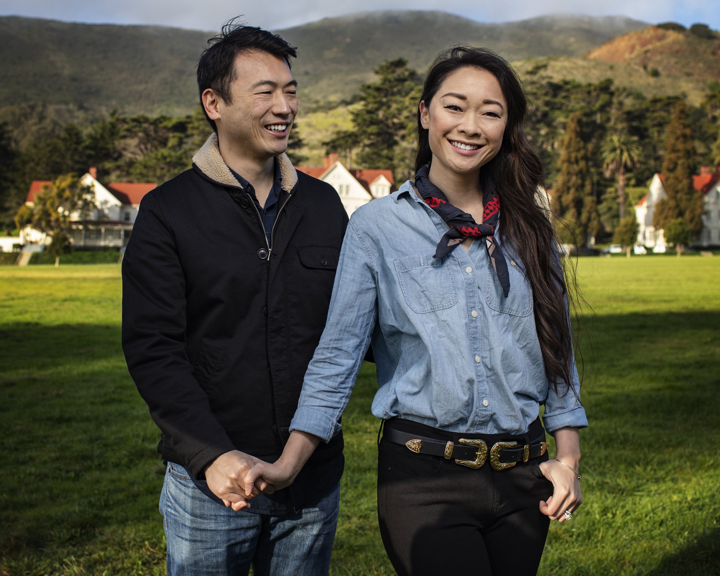 Couple holding hands and smiling in front of green hills.
