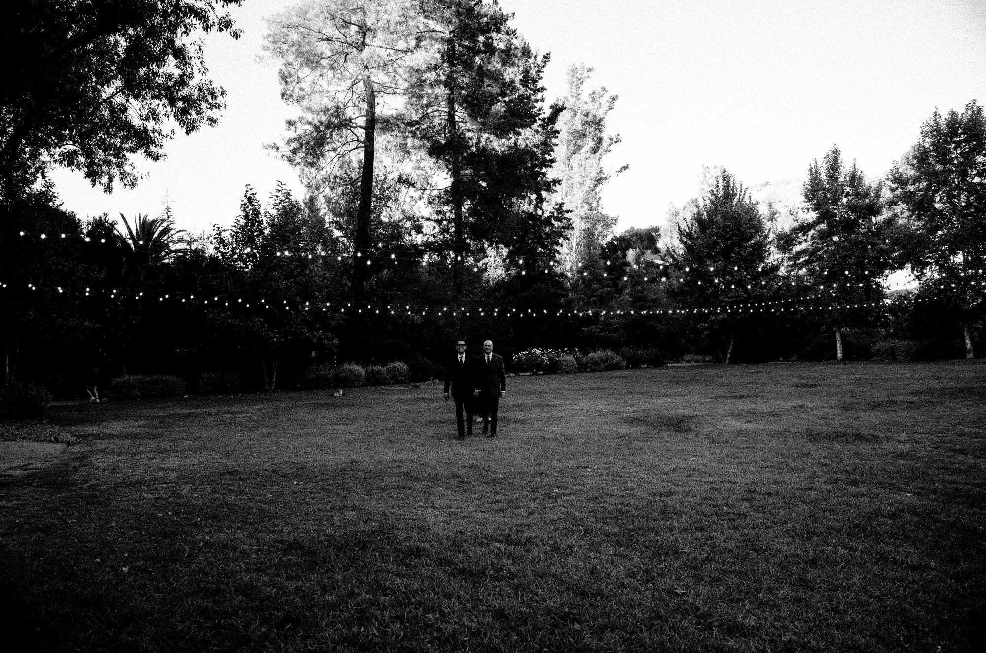 Grooms standing walking towards camera after an outdoor ceremony.