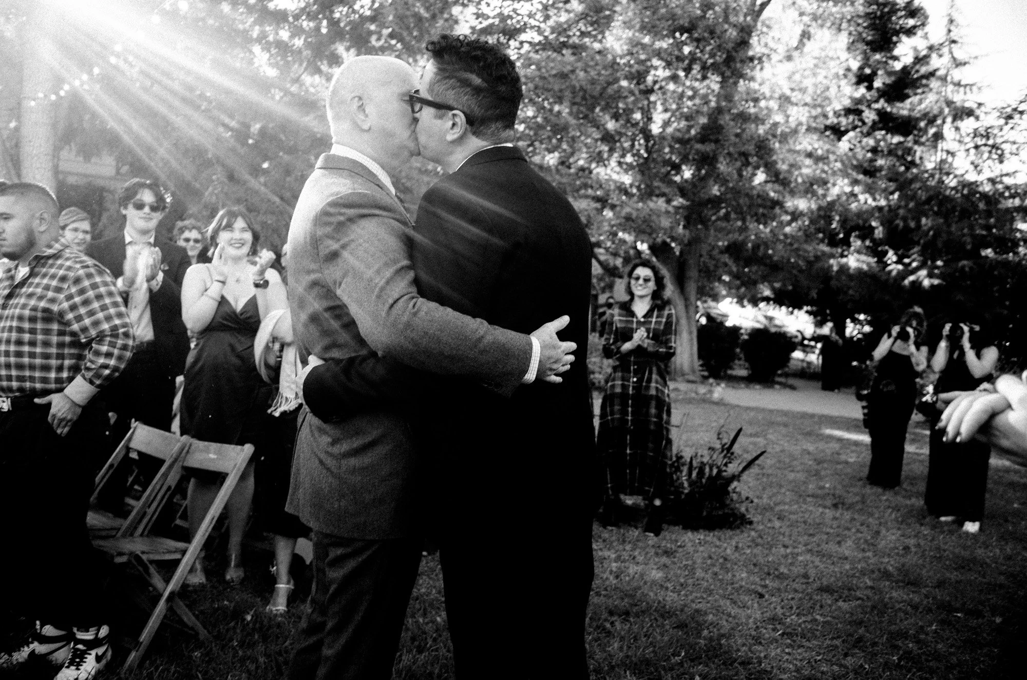 Two grooms holding each other tightly outdoors after their ceremony.
