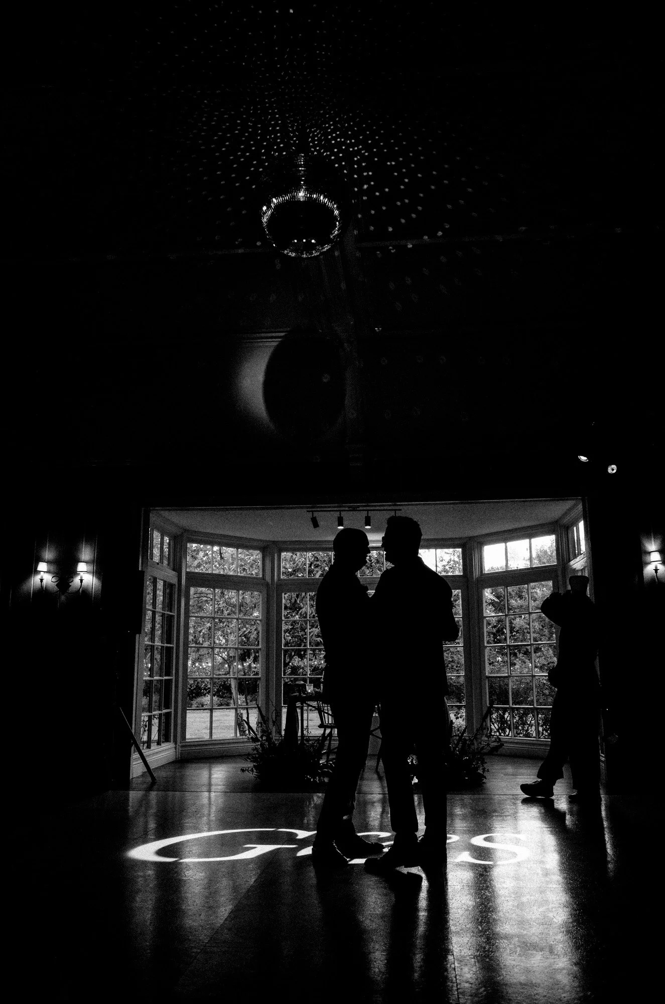 Silhouetted grooms first dance in a dark wedding venue.