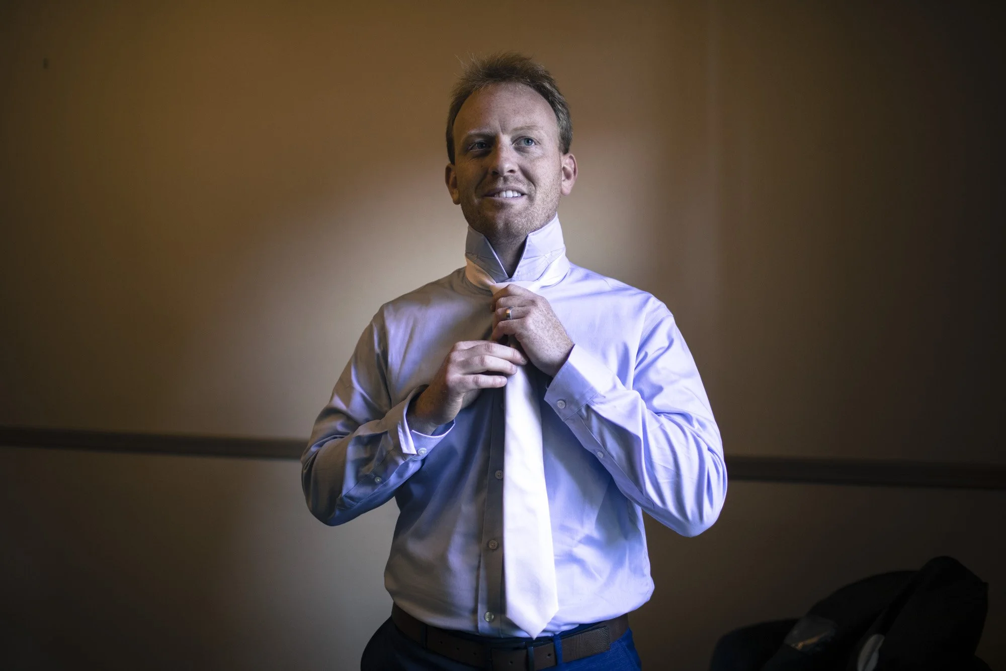 Groom adjusting his tie in a softly lit room before the wedding.
