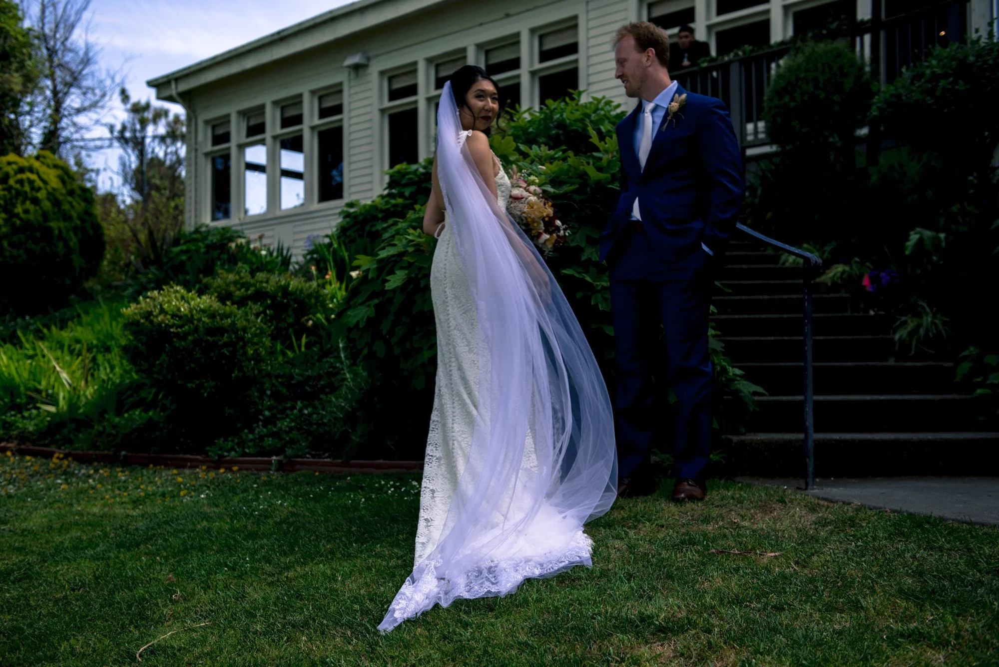 Bride and groom in a garden as her veil trails behind them.
