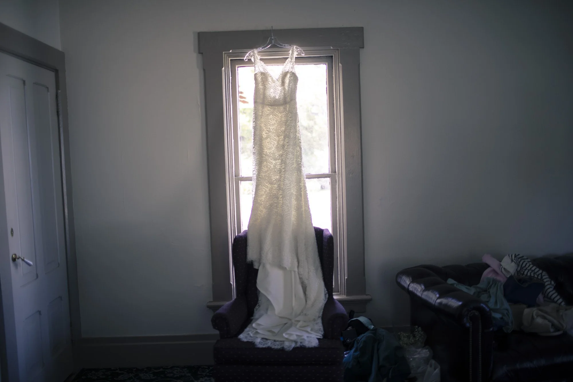 Wedding dress hanging in soft window light before the ceremony.