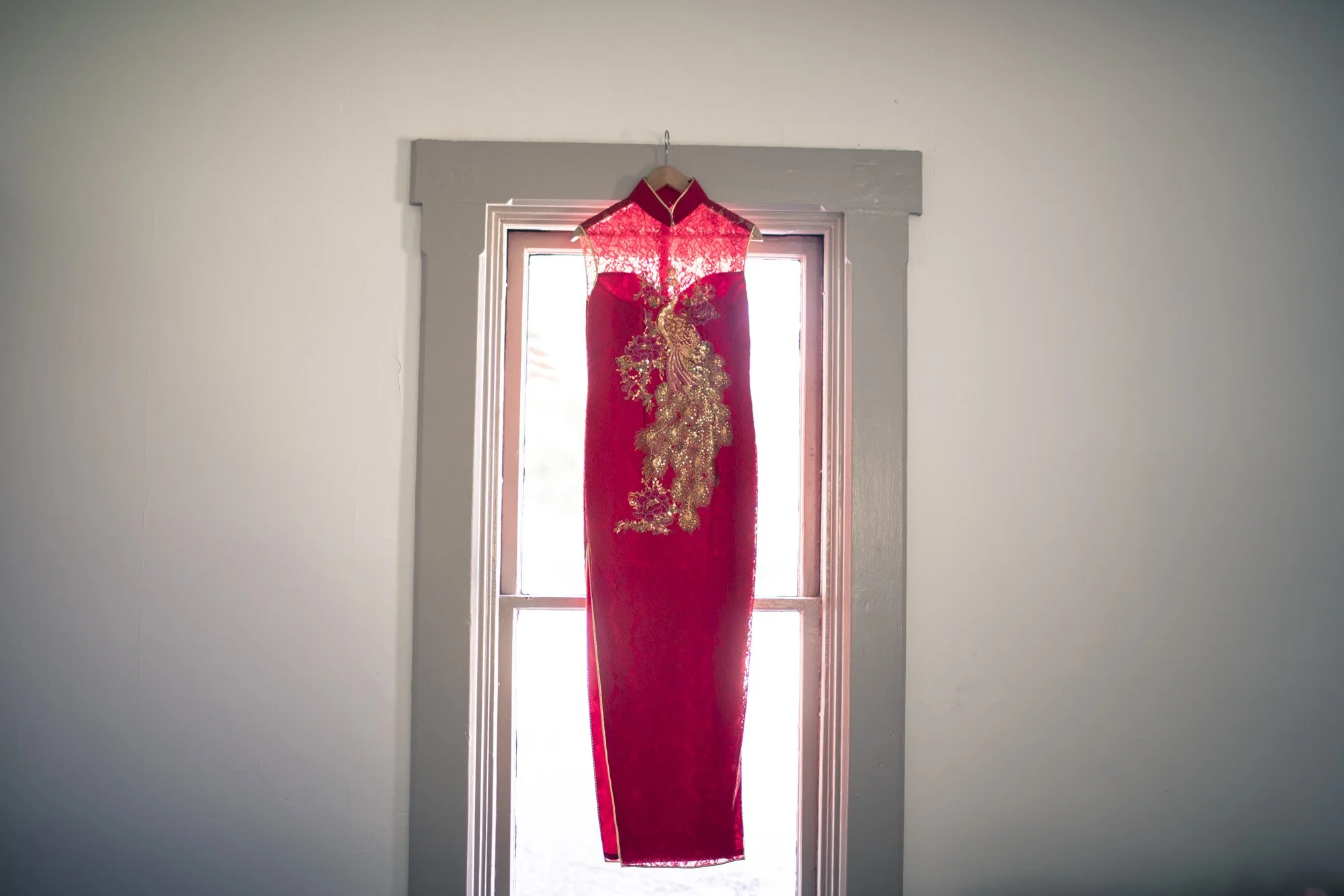 Red traditional wedding dress hanging against a bright window.