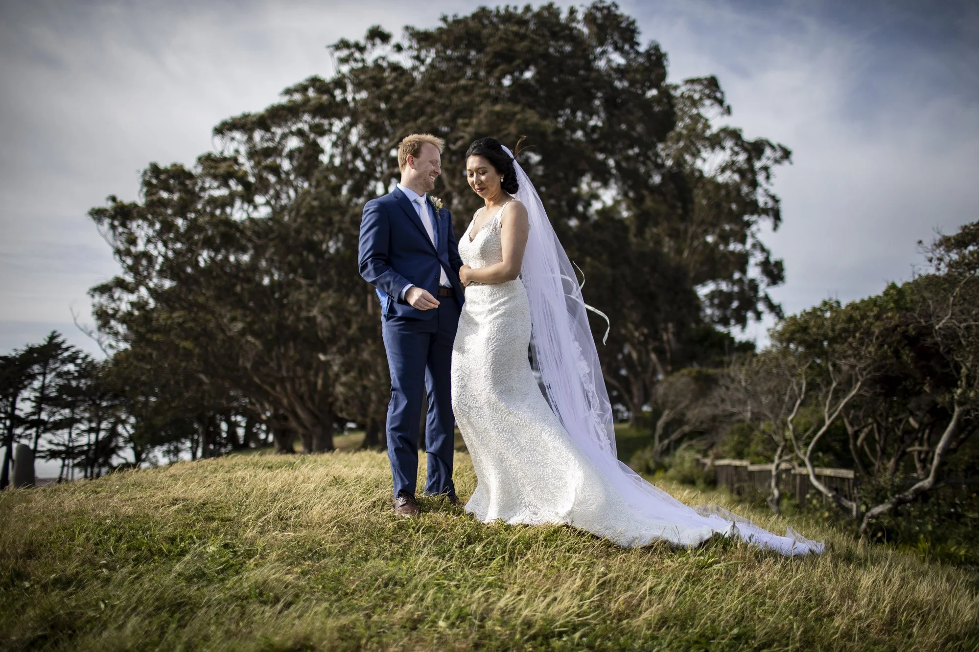 Newlyweds standing together beneath a large oak tree.