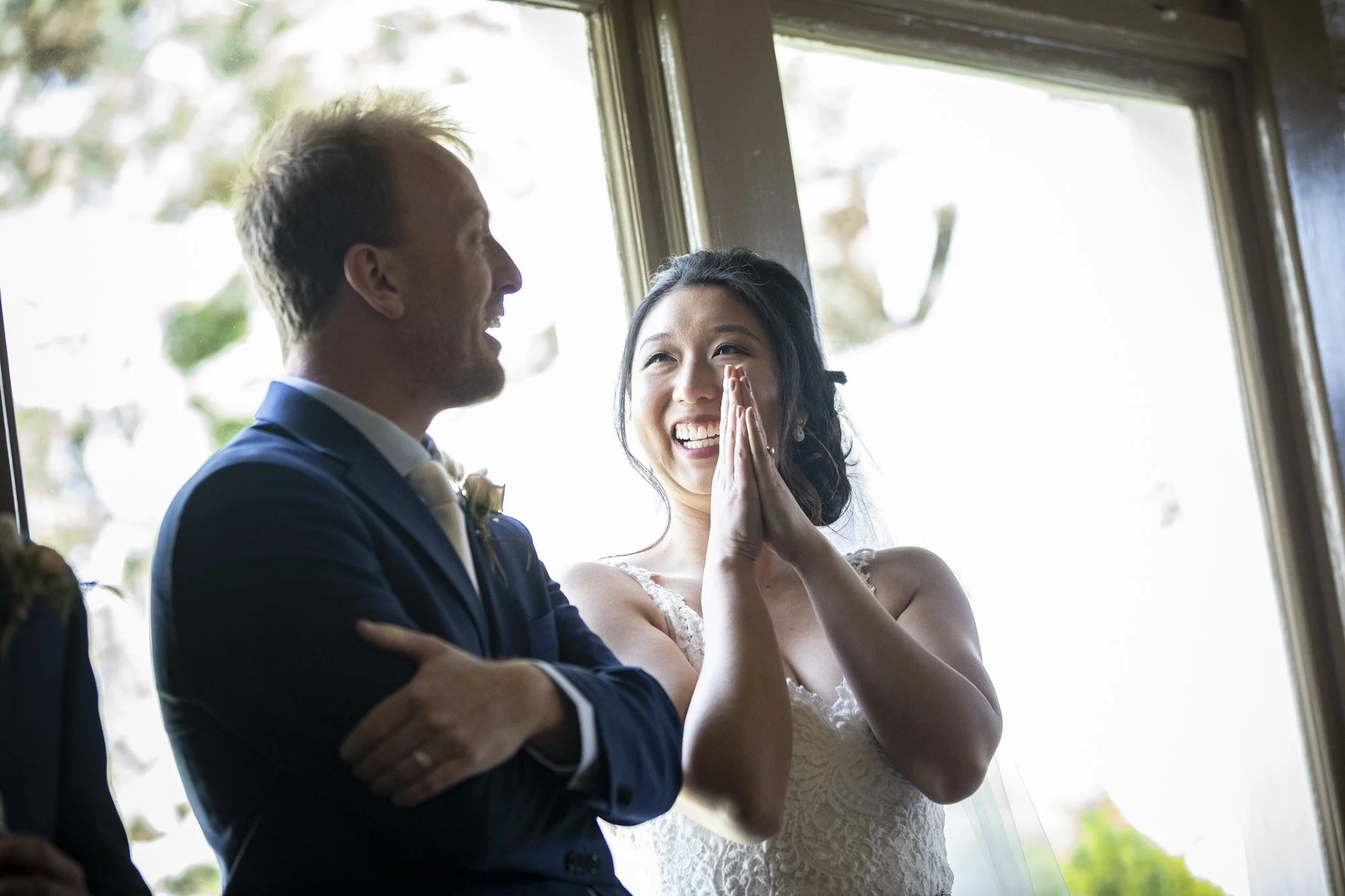 Bride touching her face with emotion beside the smiling groom.