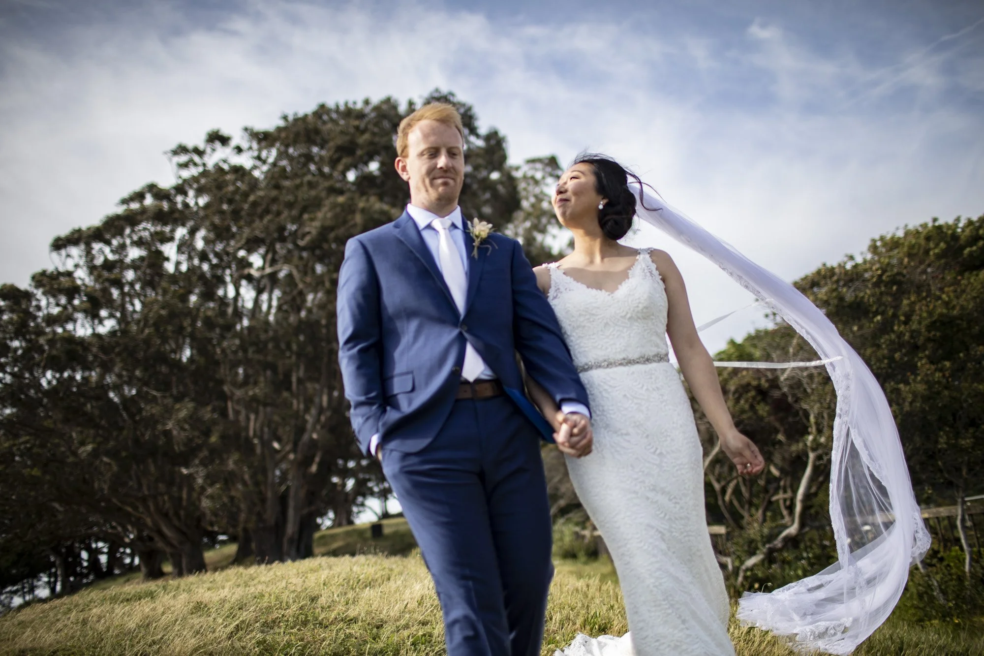 Newlyweds walking hand in hand while the bride’s veil lifts behind them.