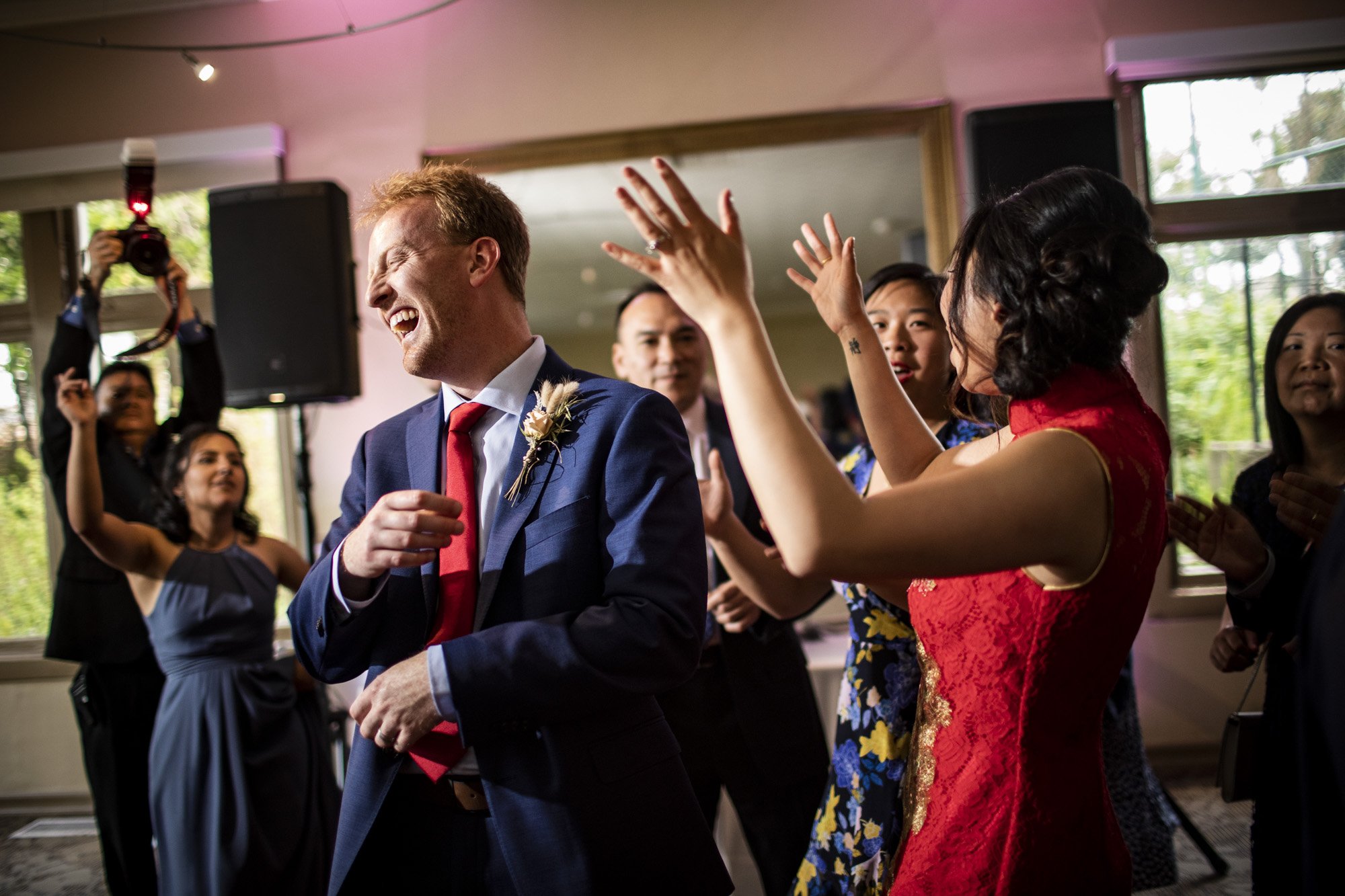 Groom dancing enthusiastically among wedding guests.