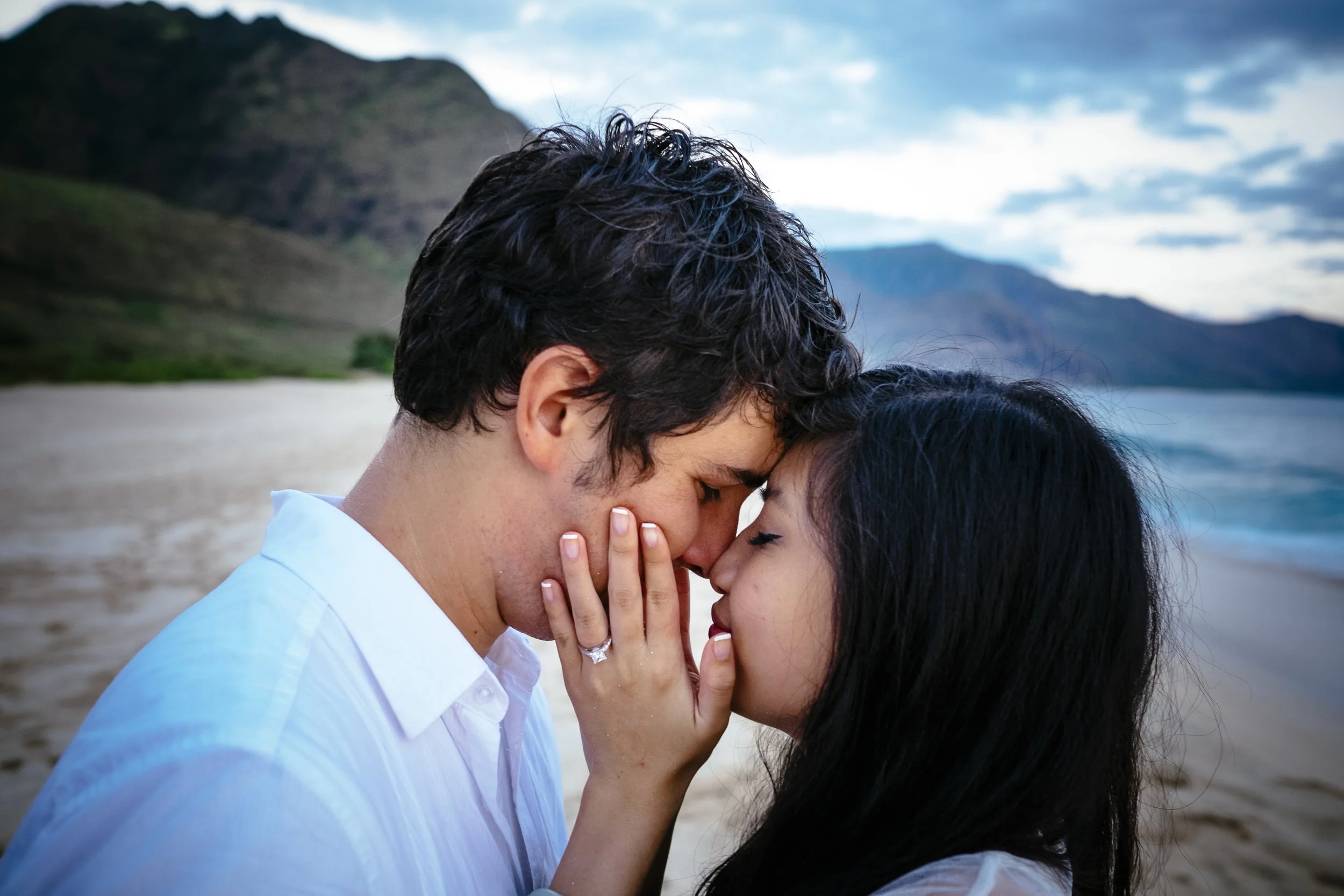 Couple kissing closely beside the ocean after their engagement.