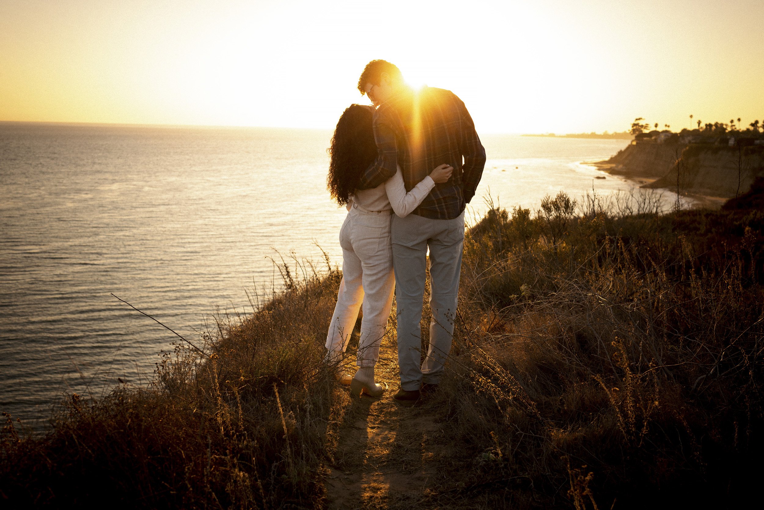 Newly engaged couple kissing in golden light above the Santa Barbara coast.