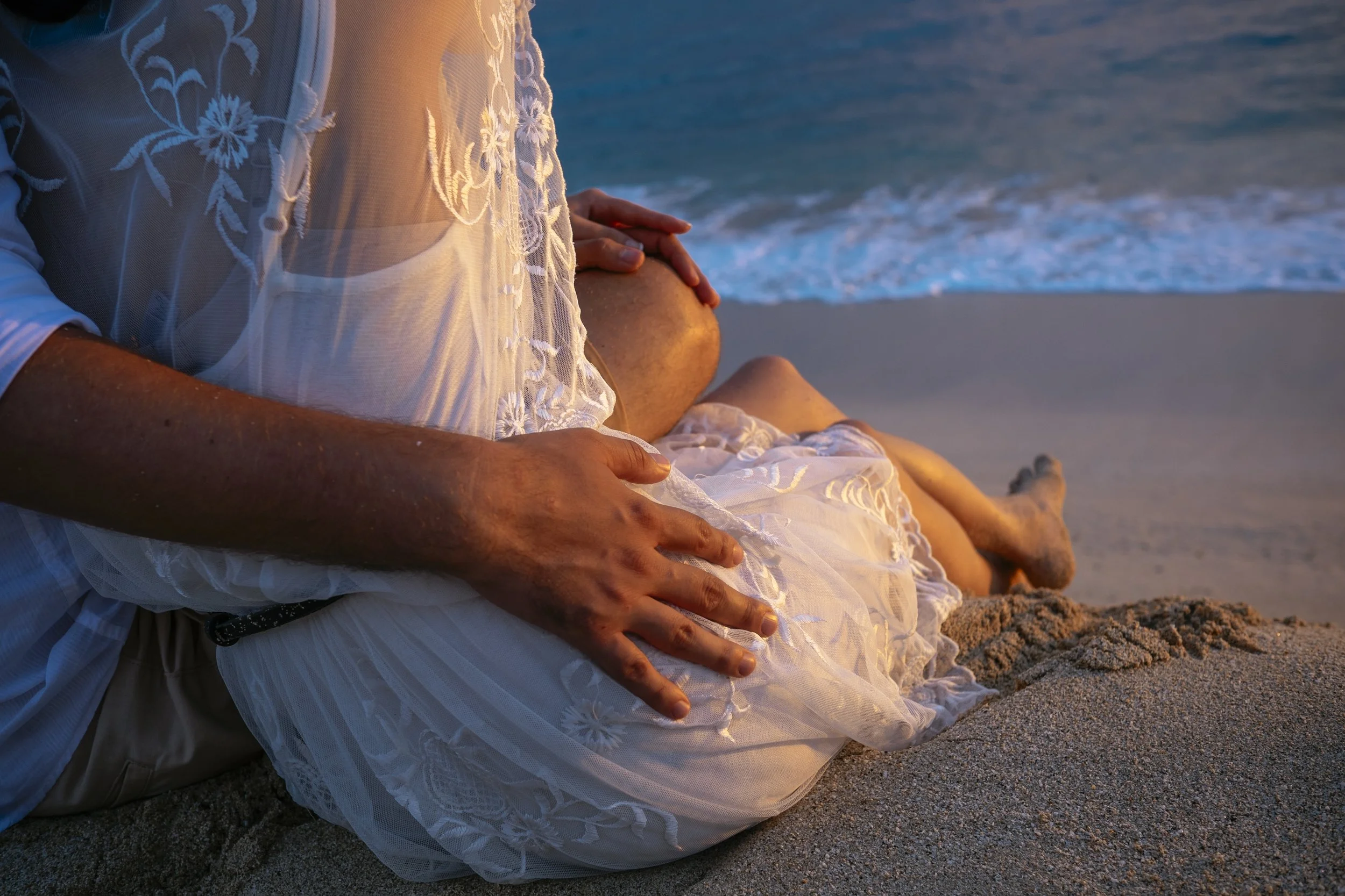 Close-up of a couple’s hands resting together on a beach.